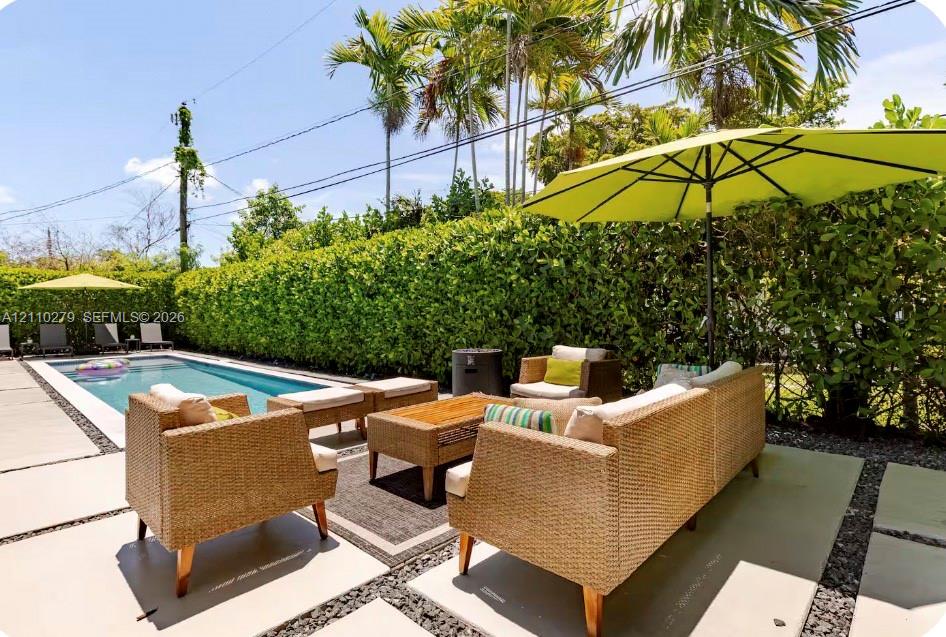 Covered patio featuring a woven reed pergola, concrete paver decking, stone aggregate inlay, and a rectangular swimming pool surrounded by a manicured hedge