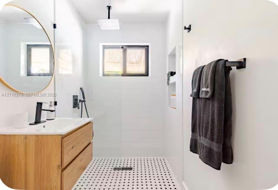 Bathroom featuring a floating wood-finish vanity, circular mirror, walk-in shower with matte black rainfall showerhead, and a built-in wall niche
