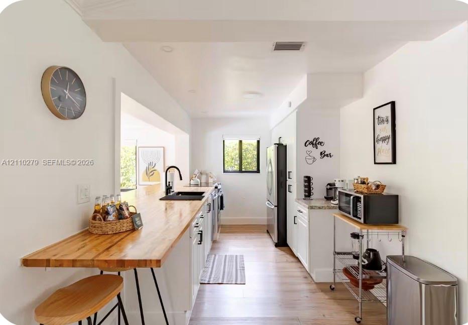 Kitchen featuring wood-finish butcher block counters, white cabinetry, integrated sink with matte black faucet, and light-toned wood-finish flooring