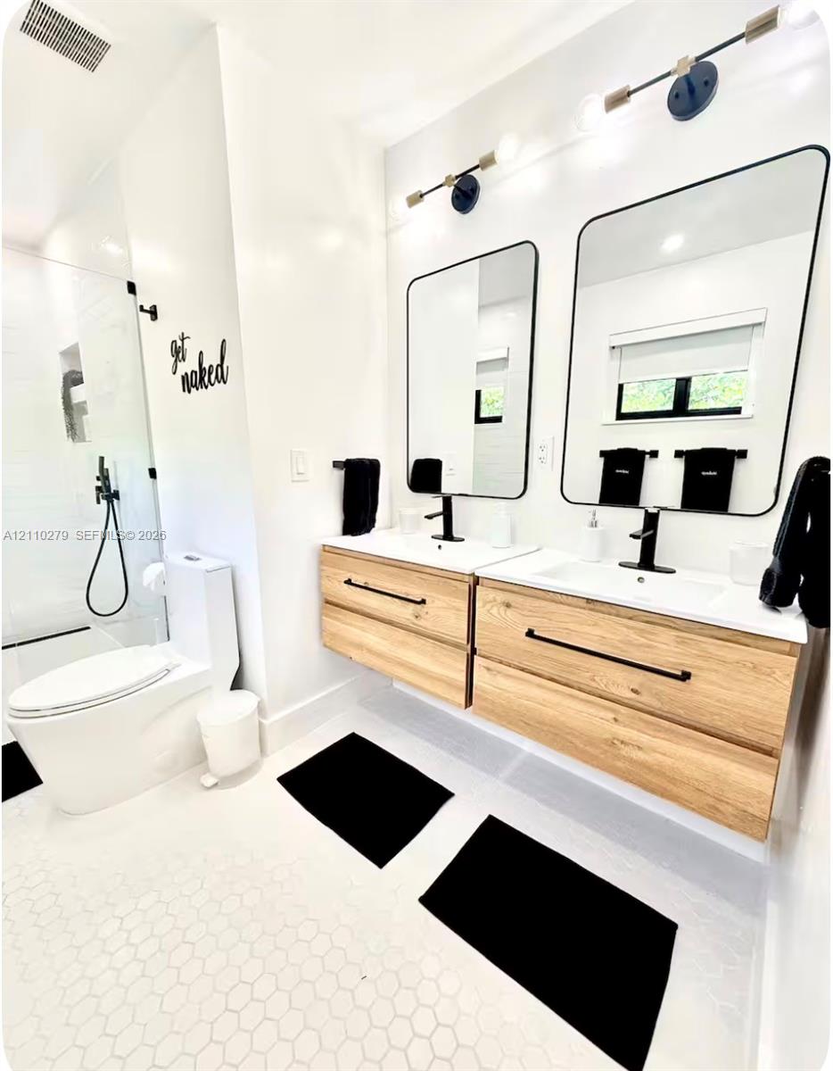 Dual floating wood-finish vanities with rectangular integrated sinks, matte black hardware, geometric mirrors, and a glass-enclosed walk-in shower
