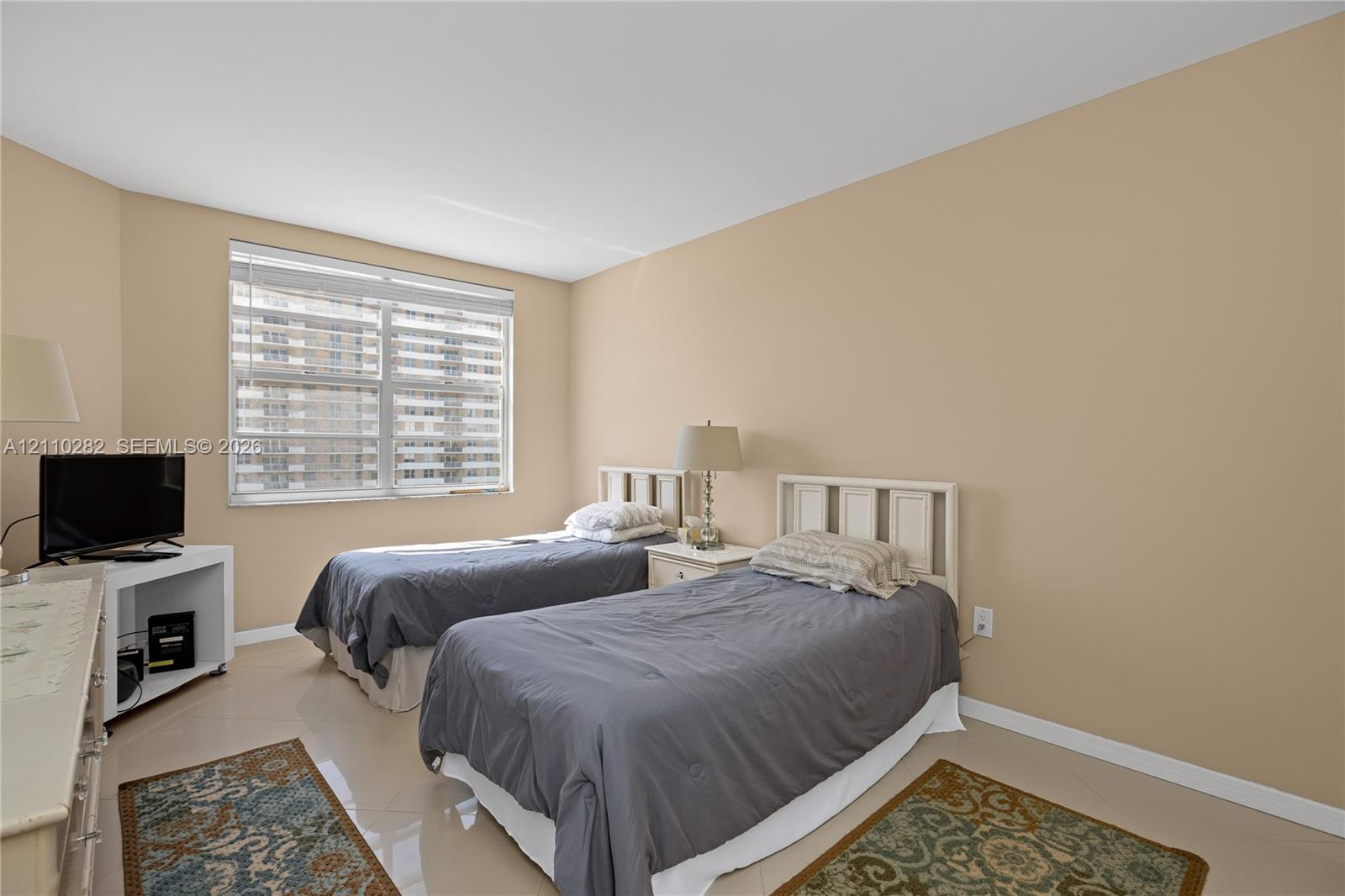 Neutral-toned room featuring large windows with fitted horizontal blinds and polished tile flooring