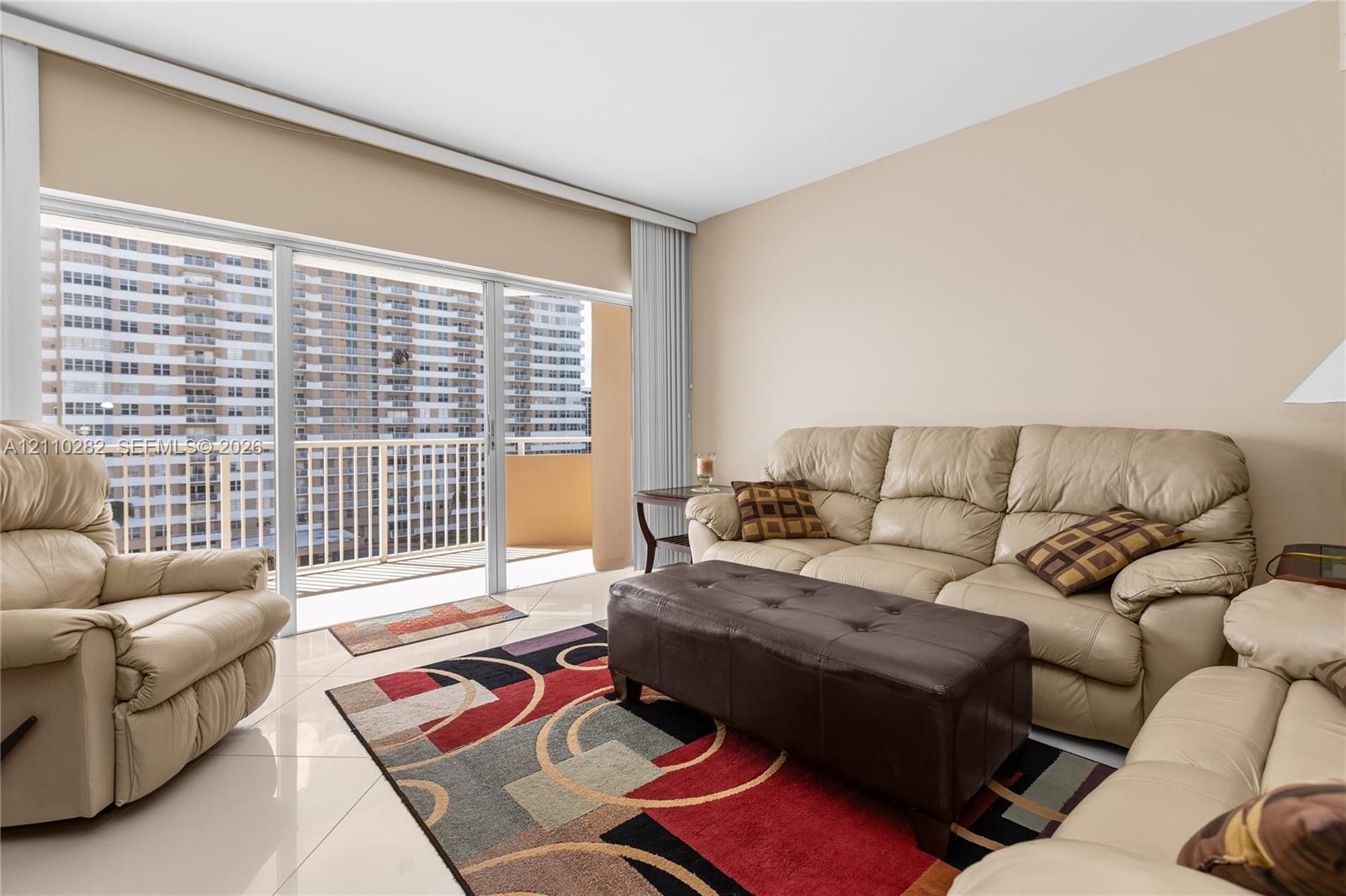 Floor-to-ceiling sliding glass doors with access to an exterior balcony, light-colored tile flooring, and vertical blinds