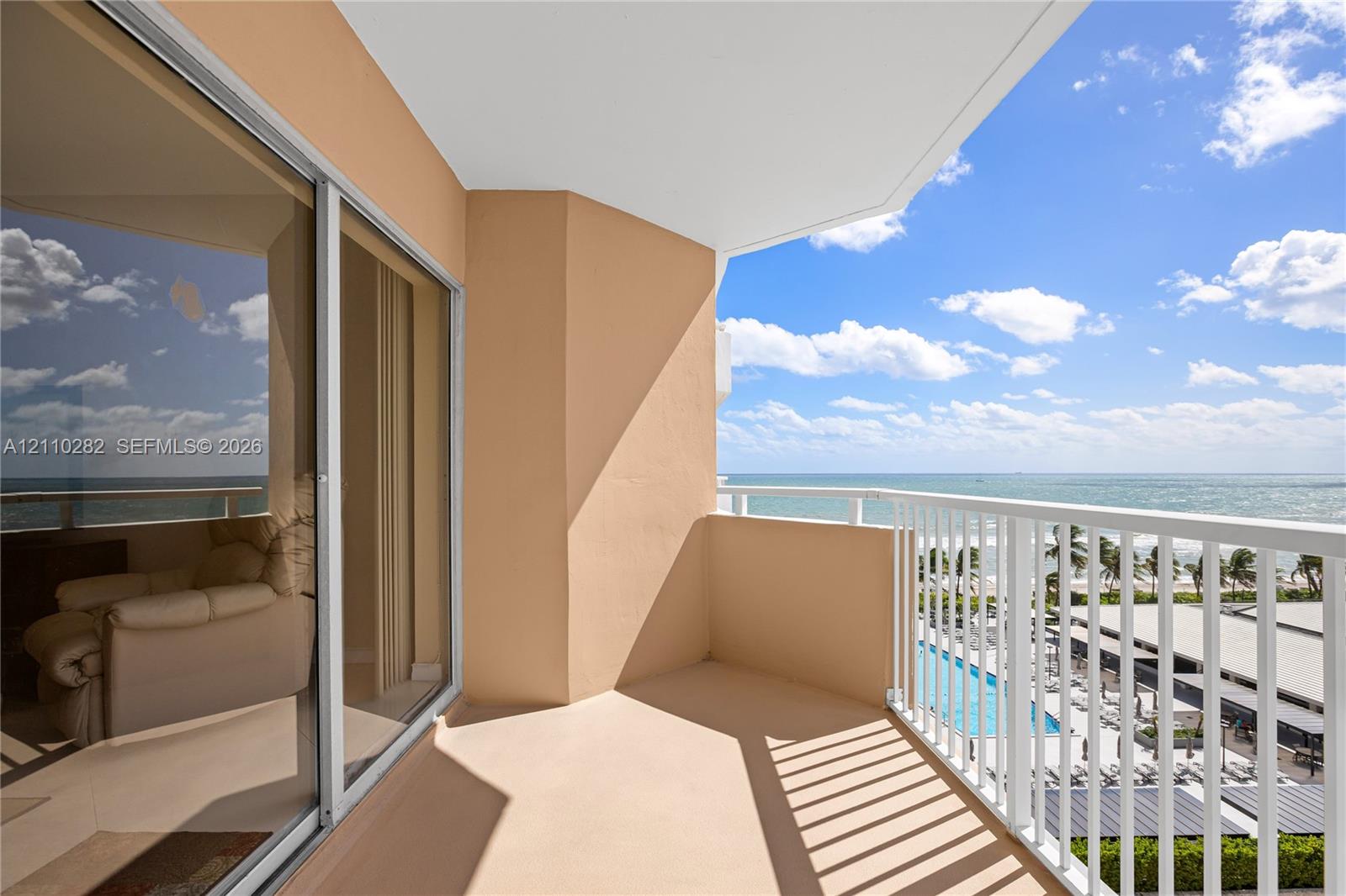 Covered balcony featuring white vertical railings, expansive glass sliding doors, and ocean frontage