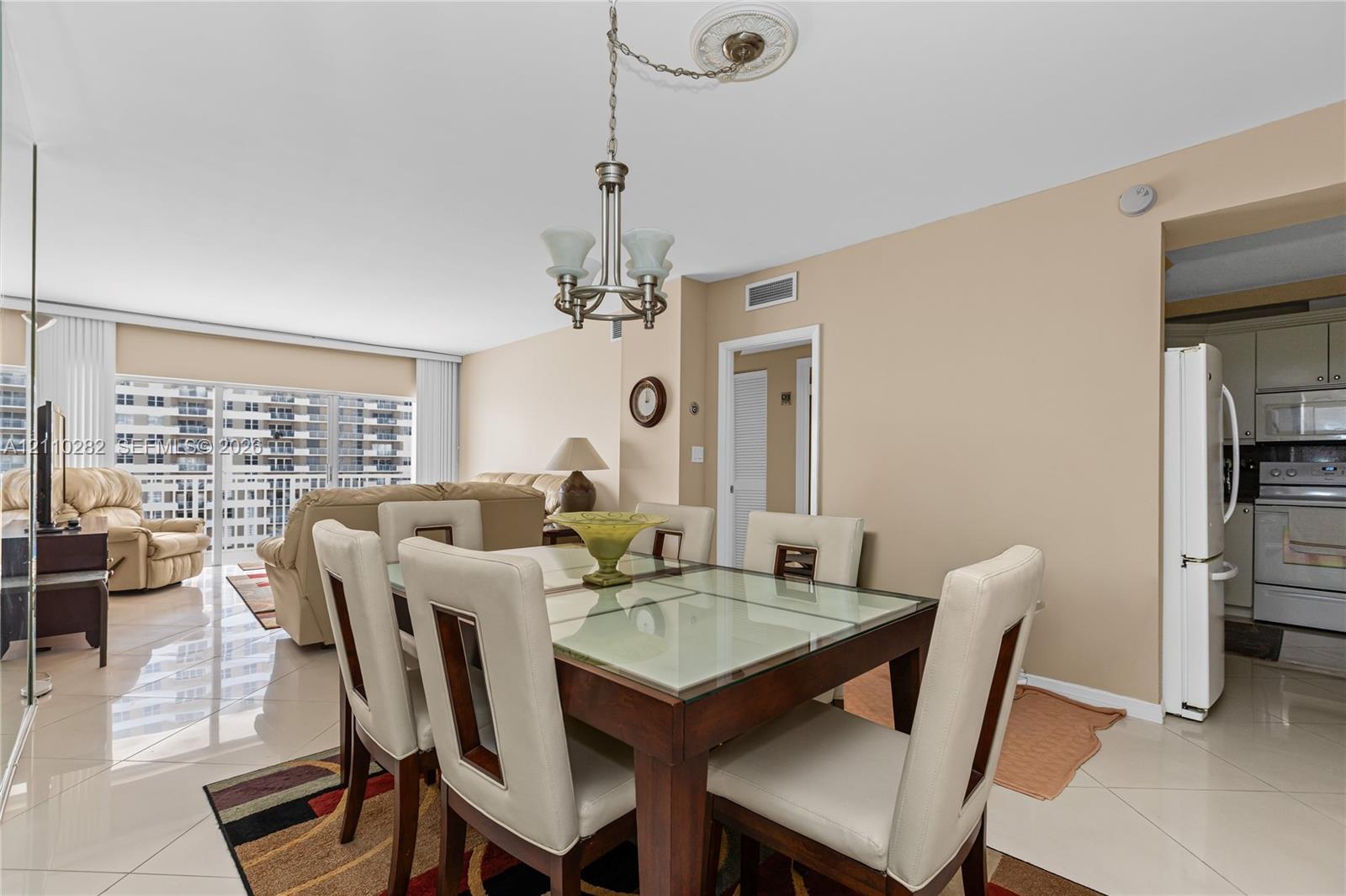 Open-concept dining area featuring polished tile flooring, a multi-light chandelier with a decorative ceiling medallion, and floor-to-ceiling glass sliding doors leading to a balcony