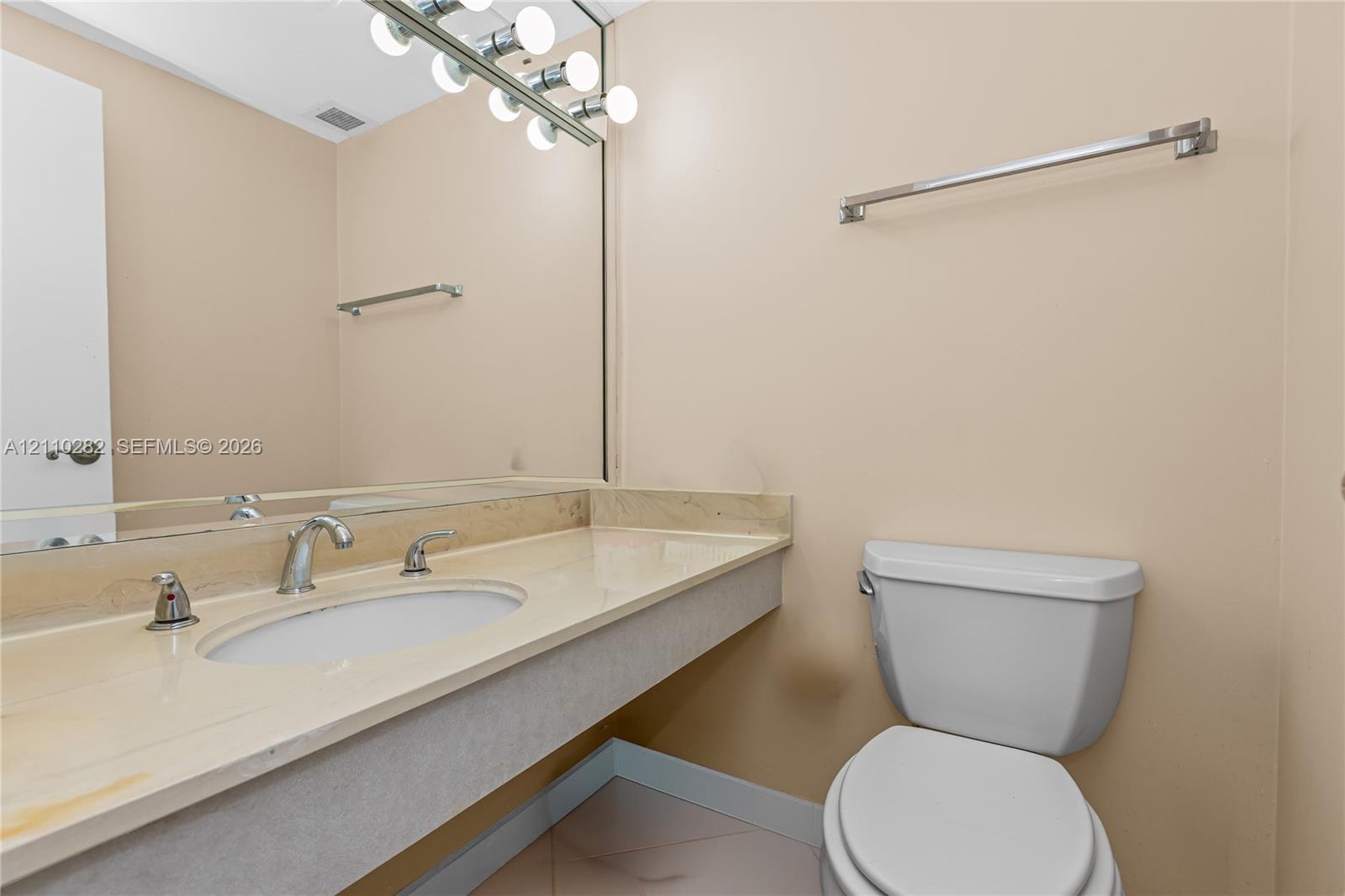 Full-width vanity with integrated sink, stone-finish countertop, polished chrome faucet, large-scale wall-mounted mirror, and multi-bulb fixture
