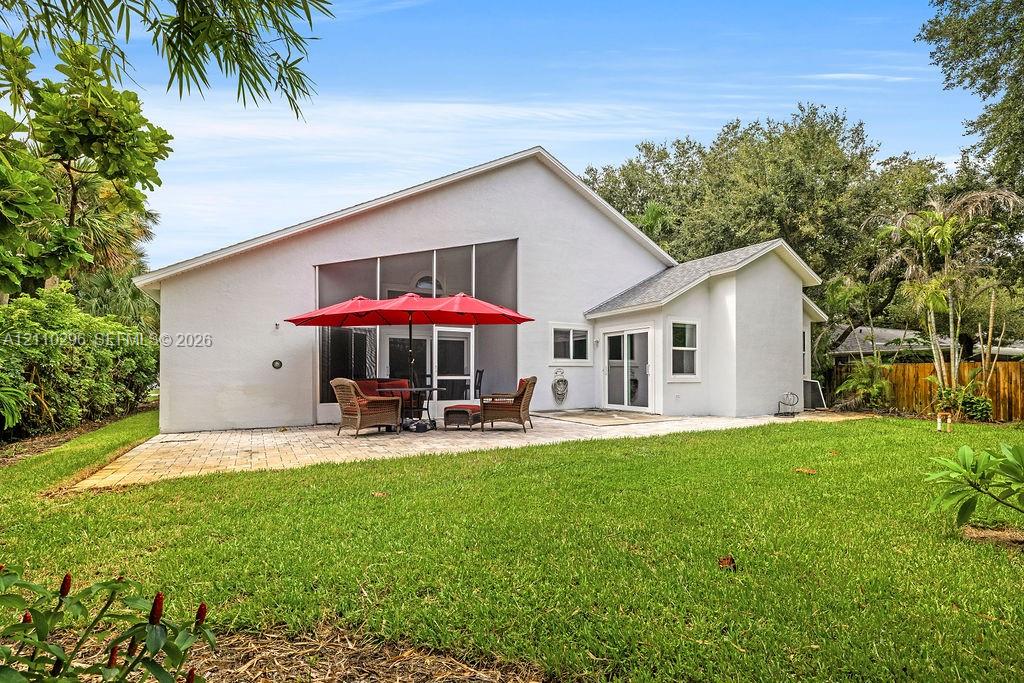 Exterior of the residence featuring a screened-in lanai, paved patio, light-colored stucco siding, and a fenced backyard with mature landscaping