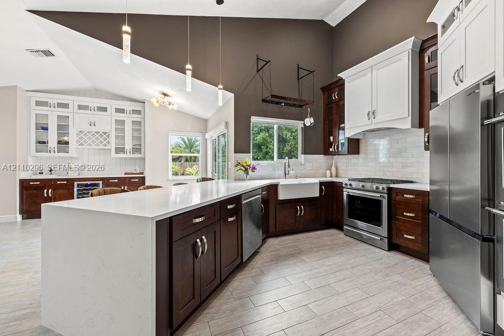 Kitchen featuring a vaulted ceiling, quartz waterfall island, dark wood-finish cabinetry, white subway tile backsplash, and farmhouse-style sink