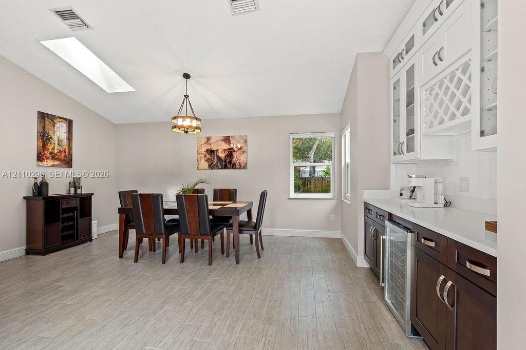 Dining area featuring wood-finish tile flooring, vaulted ceilings with a skylight, built-in cabinetry with glass-front uppers and wine storage, and a dedicated beverage refrigerator