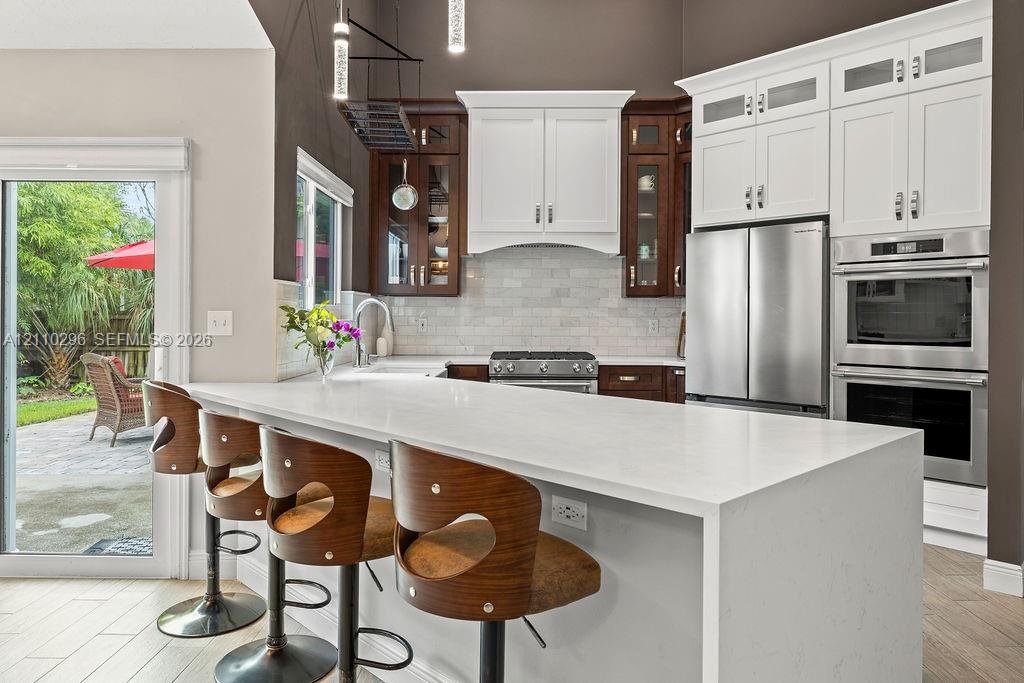 Kitchen featuring a large quartz-topped island, two-toned cabinetry, subway tile backsplash, built-in stainless steel double oven, and sliding glass door