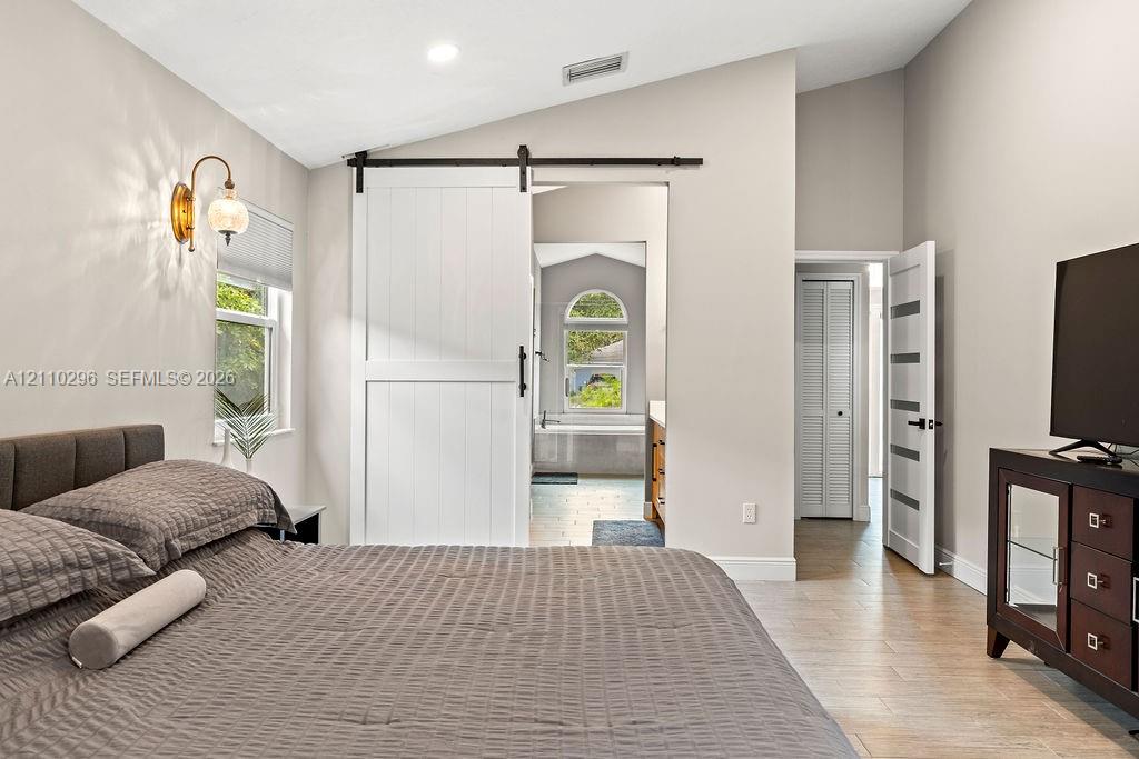 Vaulted ceiling featuring a sliding white barn door, tile flooring, wall-mounted brass light fixture, and contemporary multi-panel interior door