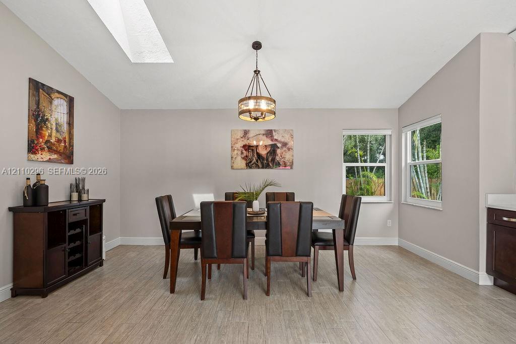 Vaulted ceiling with skylight, neutral wall tones, wood-finish flooring, and a multi-light drum pendant fixture