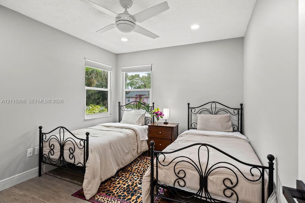 Bedroom featuring neutral wall paint, wood-finish flooring, dual windows with roller shades, and a ceiling-mounted light fixture with a fan
