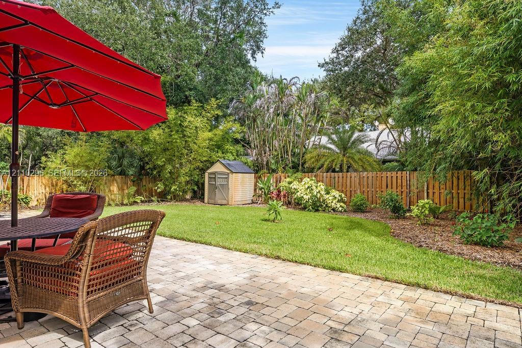Paver patio area featuring a lawn, wood-panel fencing, mature landscaping, and a detached storage structure