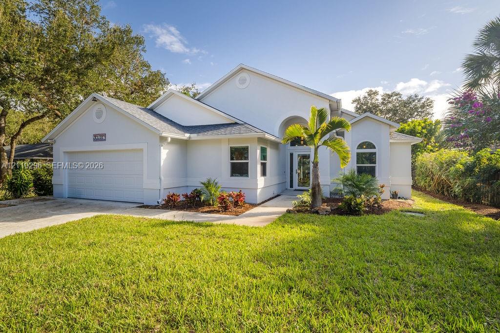 Stucco exterior with a two-car garage, arched entryway, concrete walkway, and manicured landscaping