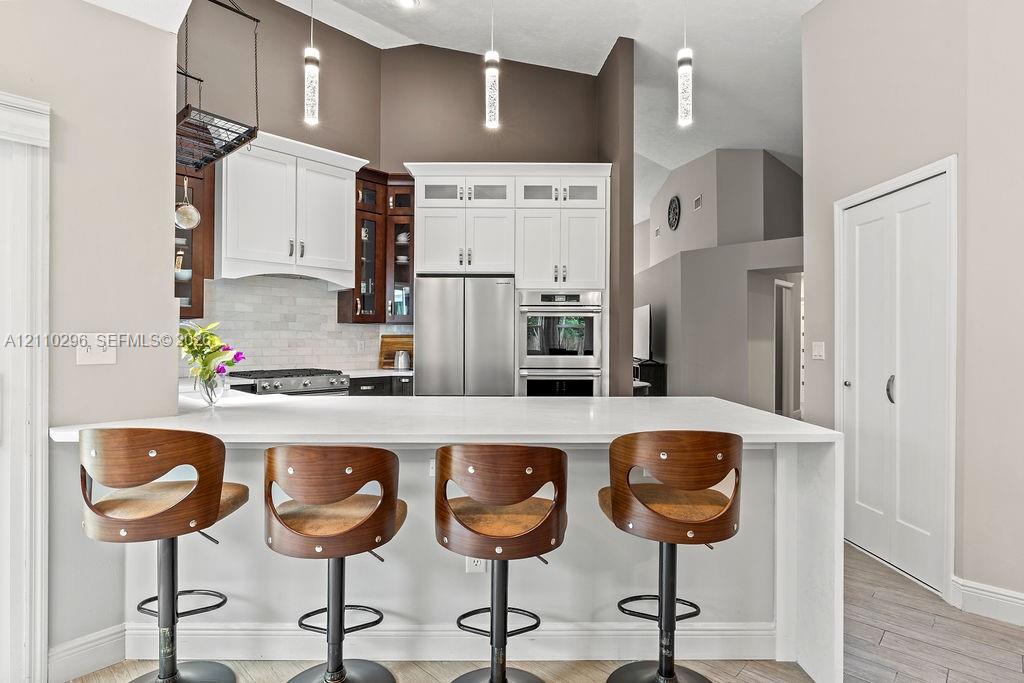 Kitchen featuring a white quartz peninsula, two-tone cabinetry with glass-front uppers, stainless steel wall oven and gas range, and three cylindrical pendant light fixtures