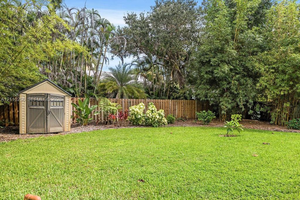 Backyard featuring a manicured lawn, wood-panel fencing, mature landscaping, and an external storage shed