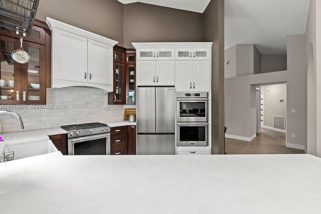 Kitchen featuring a combination of dark wood and white cabinetry, stone-finish countertops, stainless steel wall-mounted oven, and a tiled backsplash
