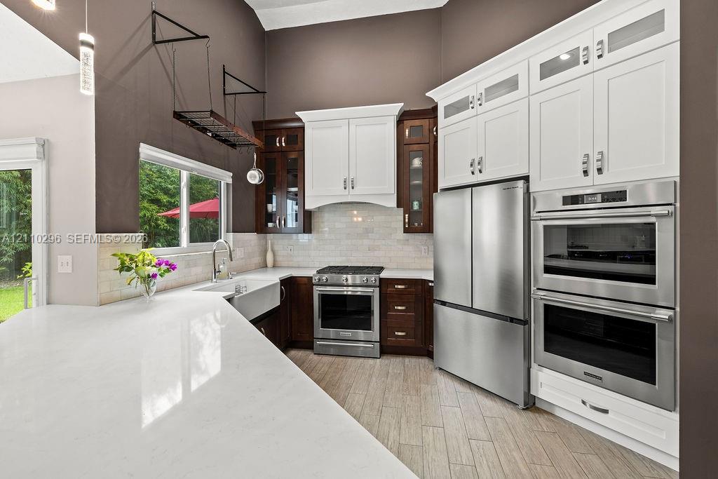 Kitchen featuring a stone-surface island, apron-front sink, stainless steel built-in double wall ovens, two-tone cabinetry, and wood-finish tile flooring