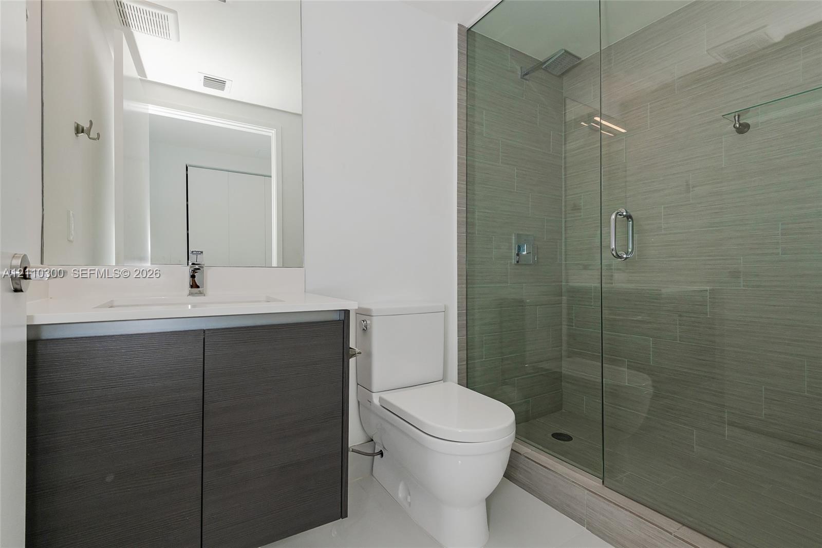Bathroom 2. Modern vanity with a countertop basin and dark wood-finish cabinetry, paired with a walk-in shower featuring a glass enclosure and textured wall tile