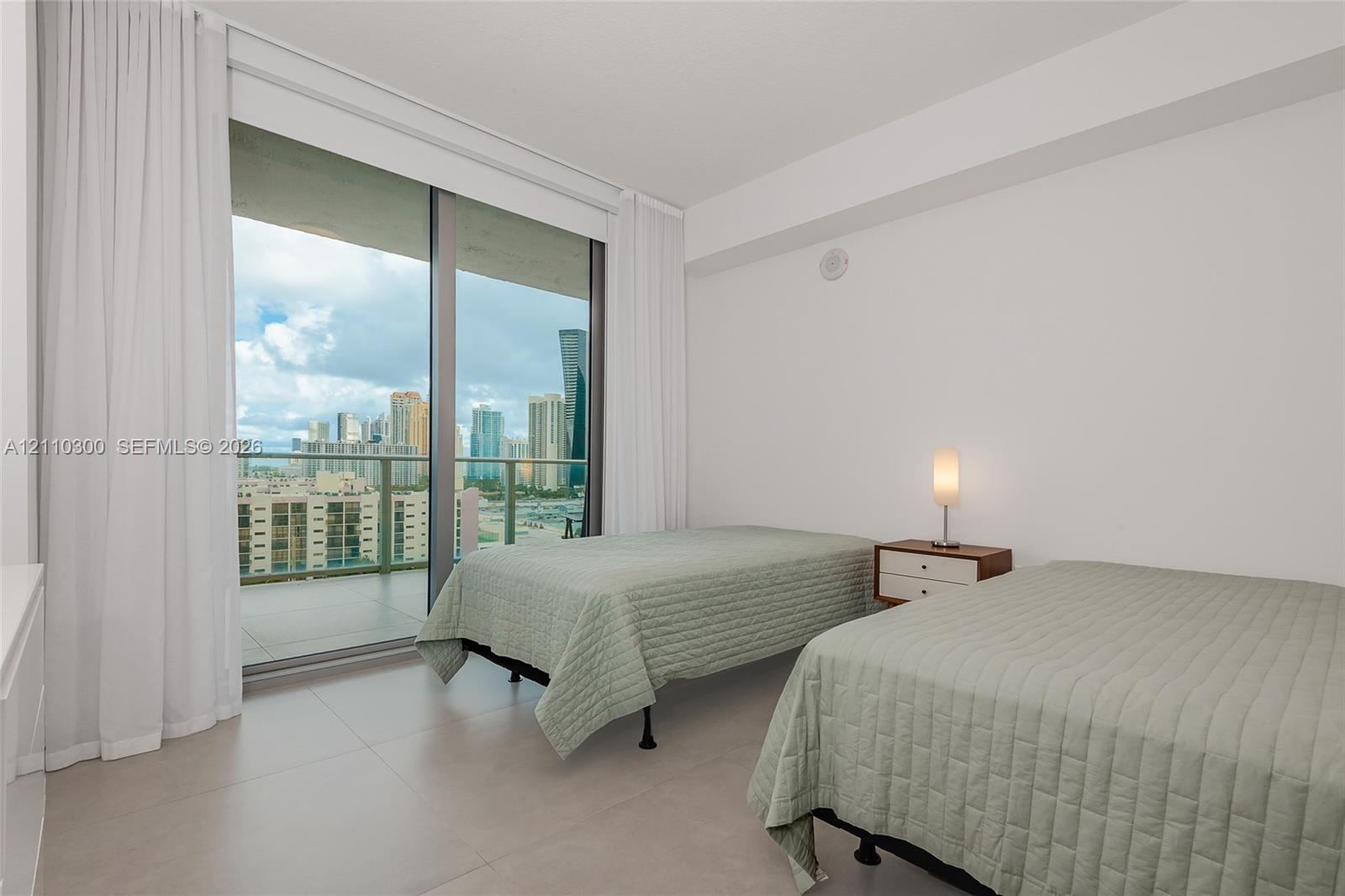 Bedroom 2. Floor-to-ceiling sliding glass door, private balcony, large format tile flooring, and urban skyline backdrop