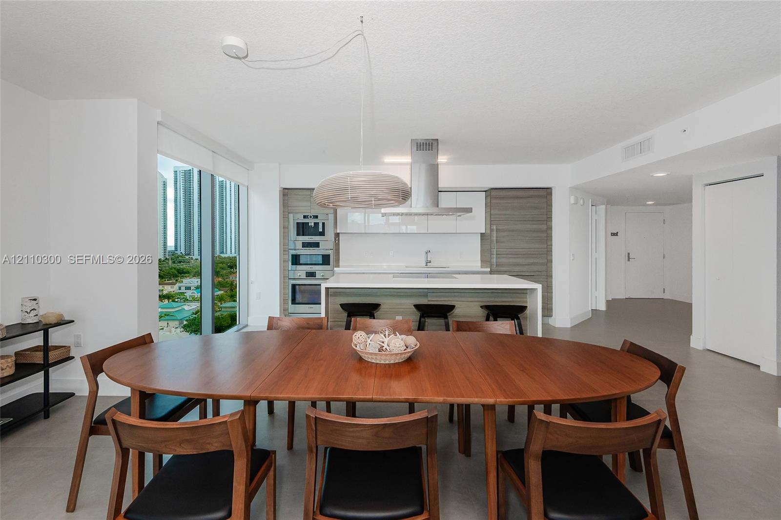 Kitchen featuring horizontal grain wood-finish cabinetry, a central island with a solid surface countertop, stainless steel built-in double ovens, and a stainless steel range hood