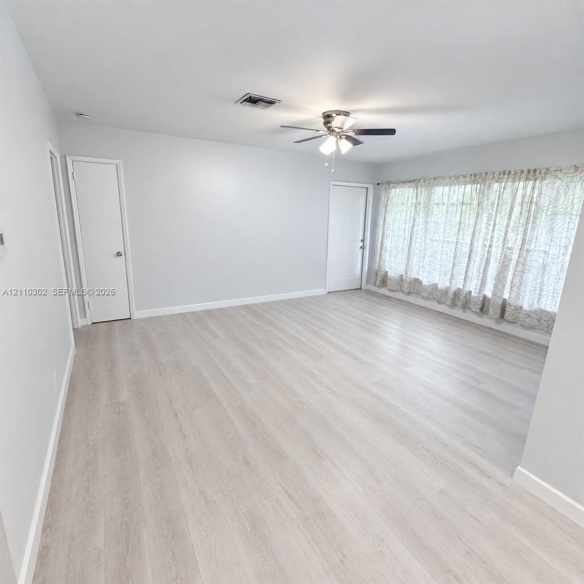 Neutral interior space featuring wood-finish flooring, a ceiling fan with integrated lighting, and expansive window coverage