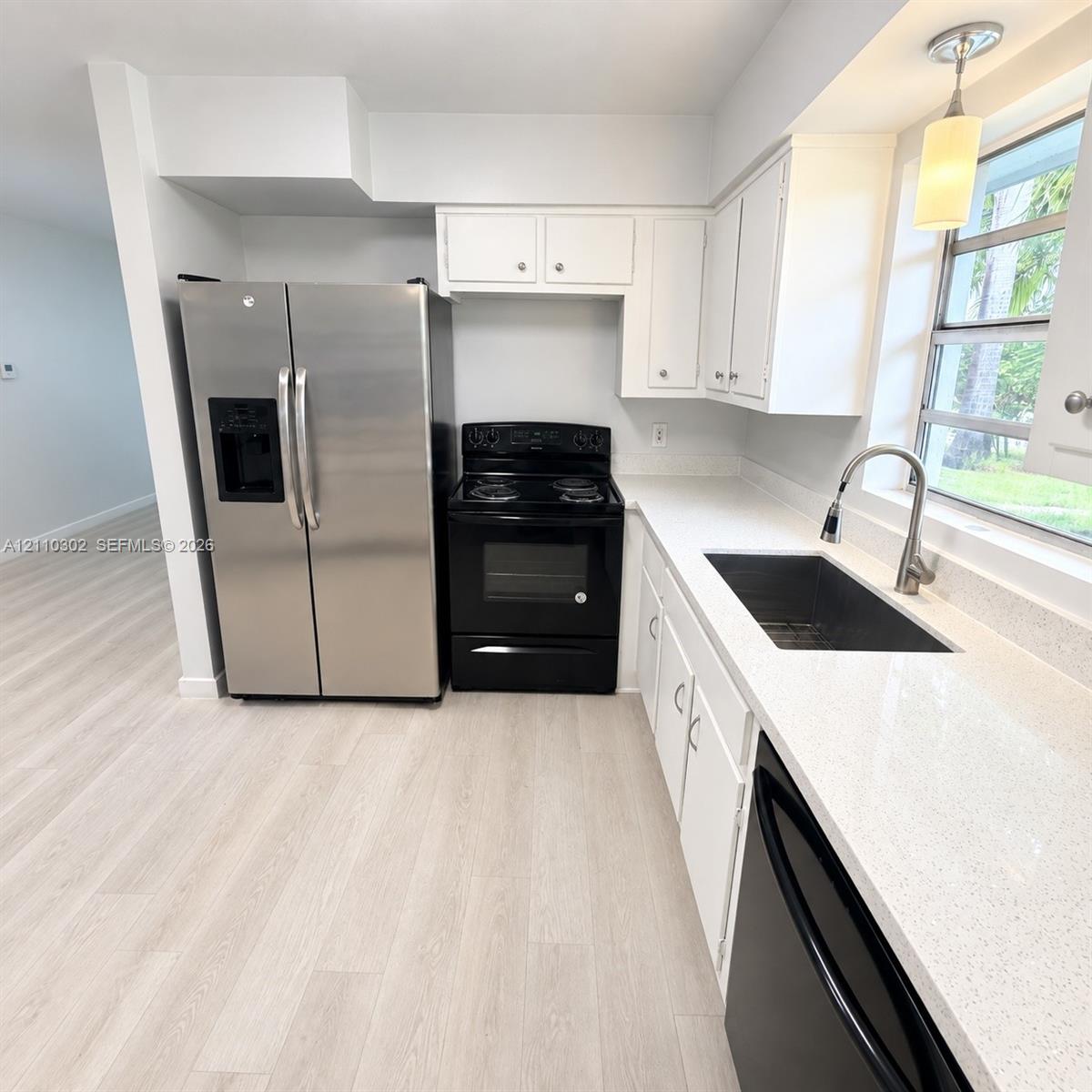 Kitchen featuring white cabinetry, light-toned solid surface countertops, stainless steel side-by-side refrigerator, black electric range, and wood-finish flooring