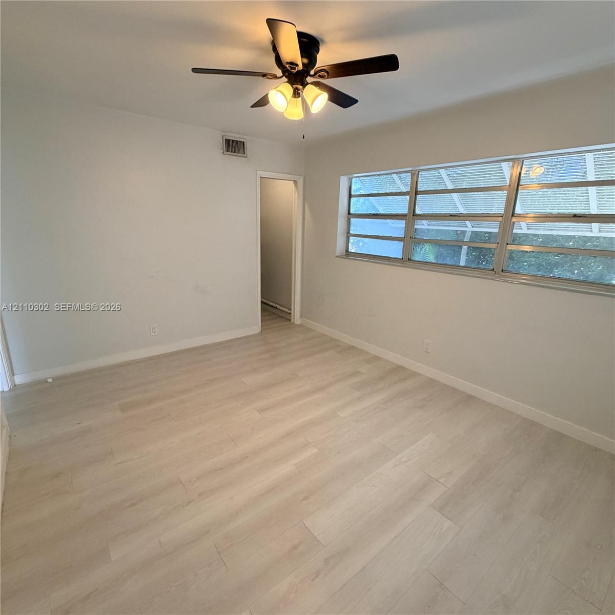 Neutral-toned wood-finish flooring, multi-pane horizontal sliding windows, and a ceiling-mounted light fixture with a five-blade fan