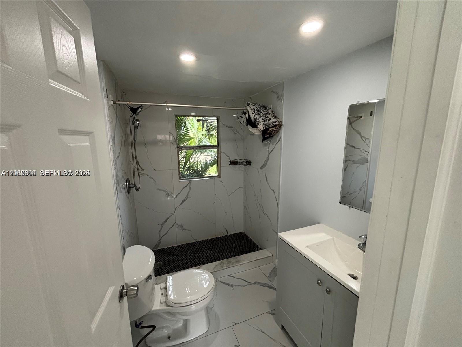 Bathroom featuring large-format stone-patterned tile, walk-in shower with rainfall showerhead, vanity with integrated sink, and recessed lighting