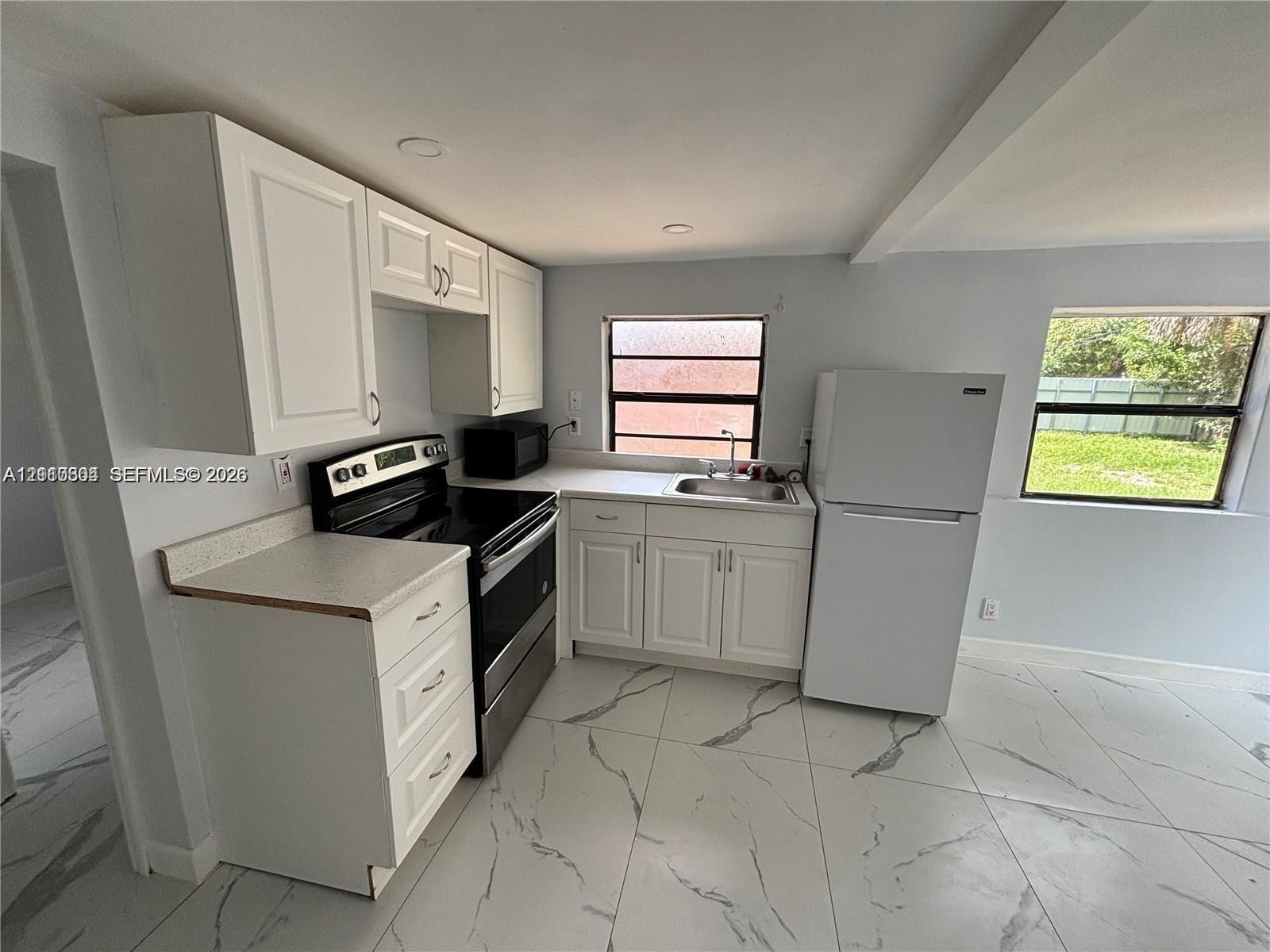Kitchen featuring white shaker-style cabinetry, neutral stone-finish countertops, stainless steel electric range, and large-format porcelain tile flooring