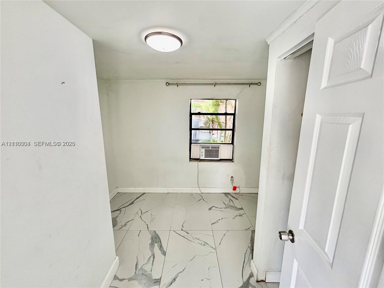 Large-format veined tile flooring, flush-mount circular lighting fixture, and a single-hung window with a mounted window air conditioning unit