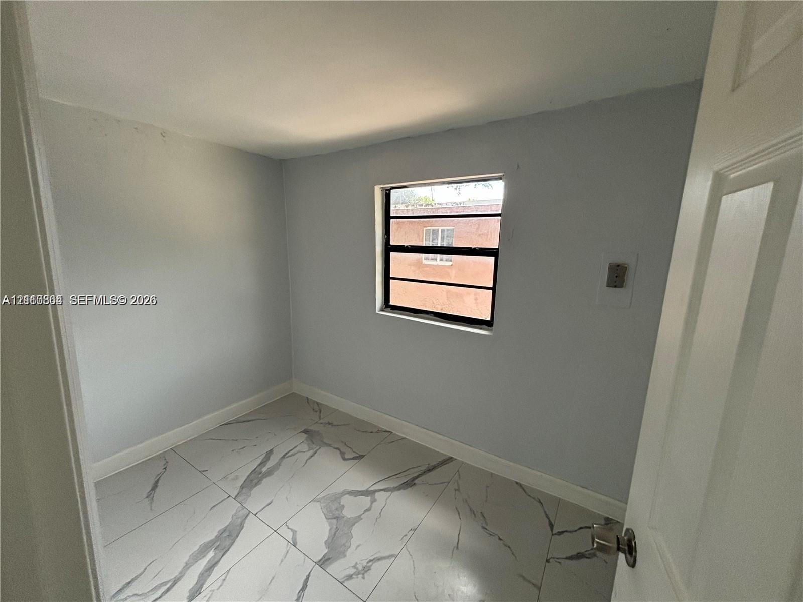 Interior space featuring large-format light-toned tile flooring with veining, neutral wall paint, and a single-pane horizontal sliding window