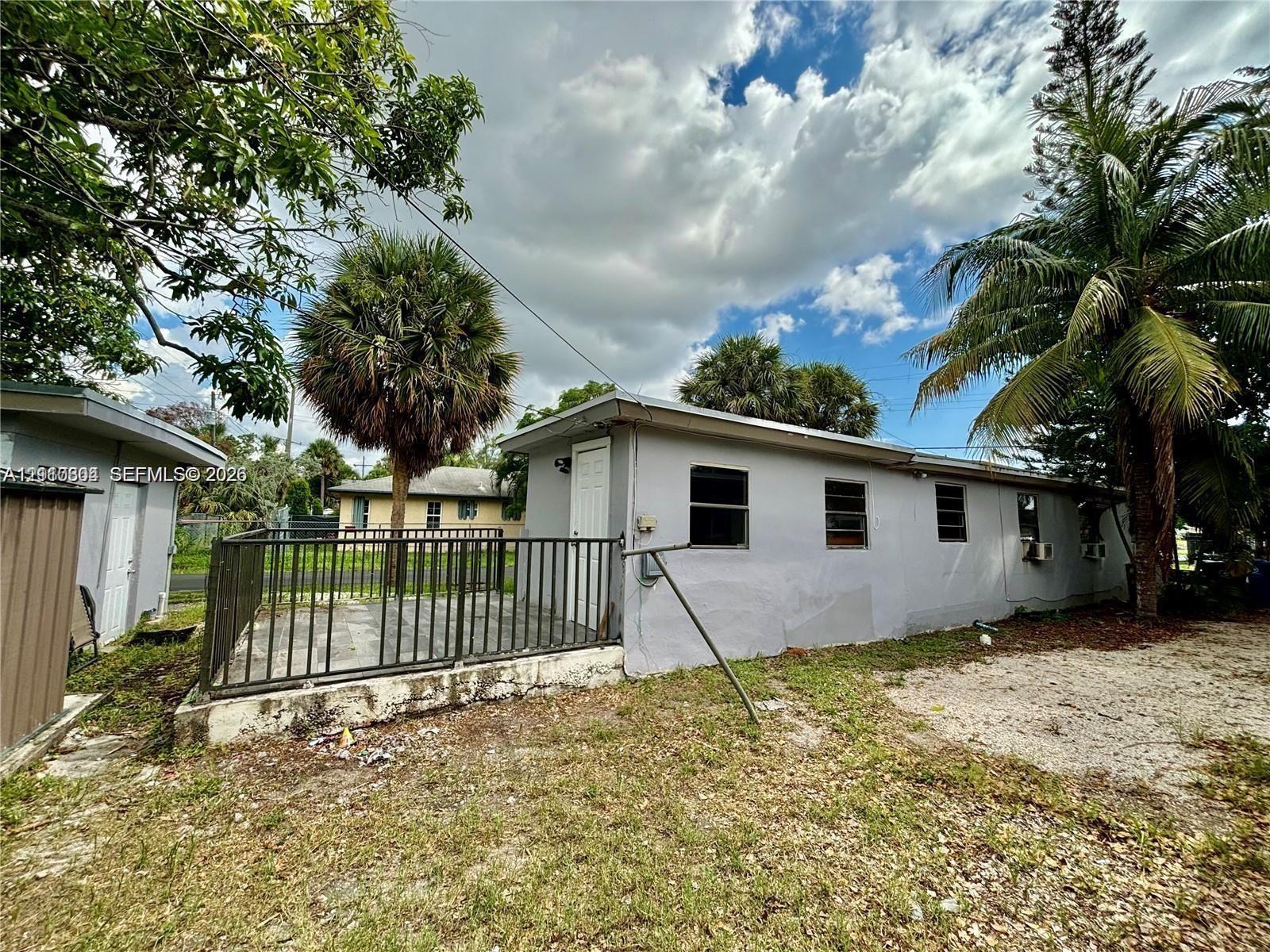 Exterior space featuring a concrete patio enclosed by metal fencing, neutral-toned stucco siding, and mature palm trees