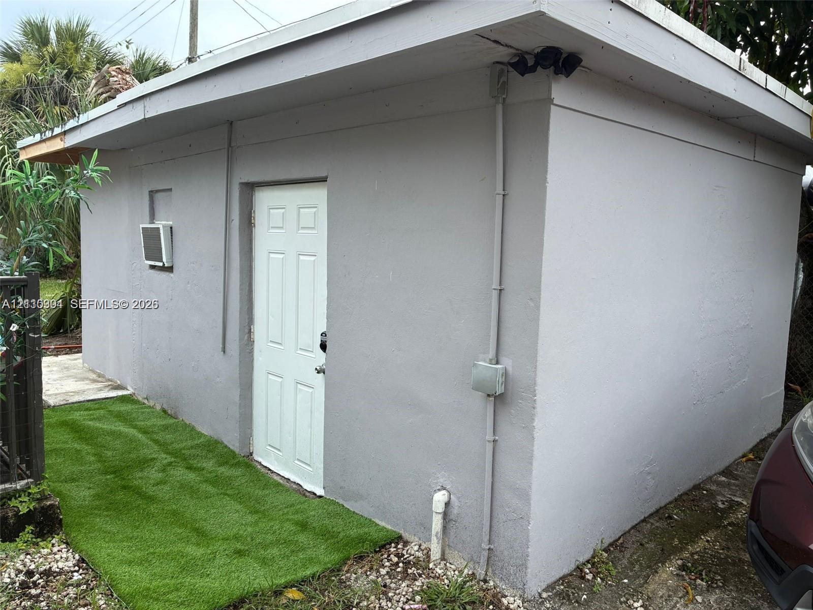 Detached structure featuring a textured stucco exterior, a single-panel entry door, and an integrated exterior lighting fixture