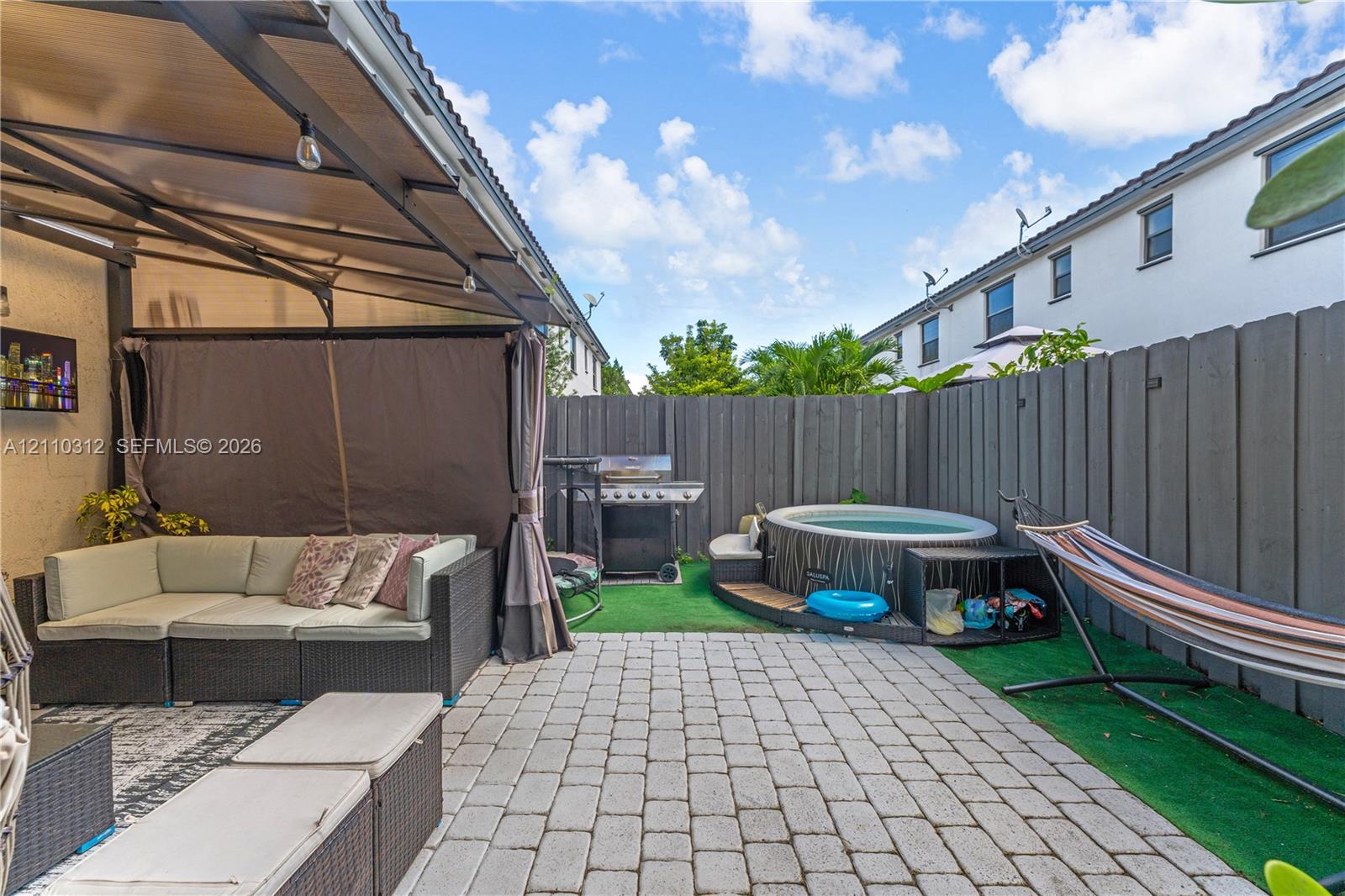 Enclosed patio area featuring stone paver flooring, a metal-framed overhead canopy, and a privacy fence
