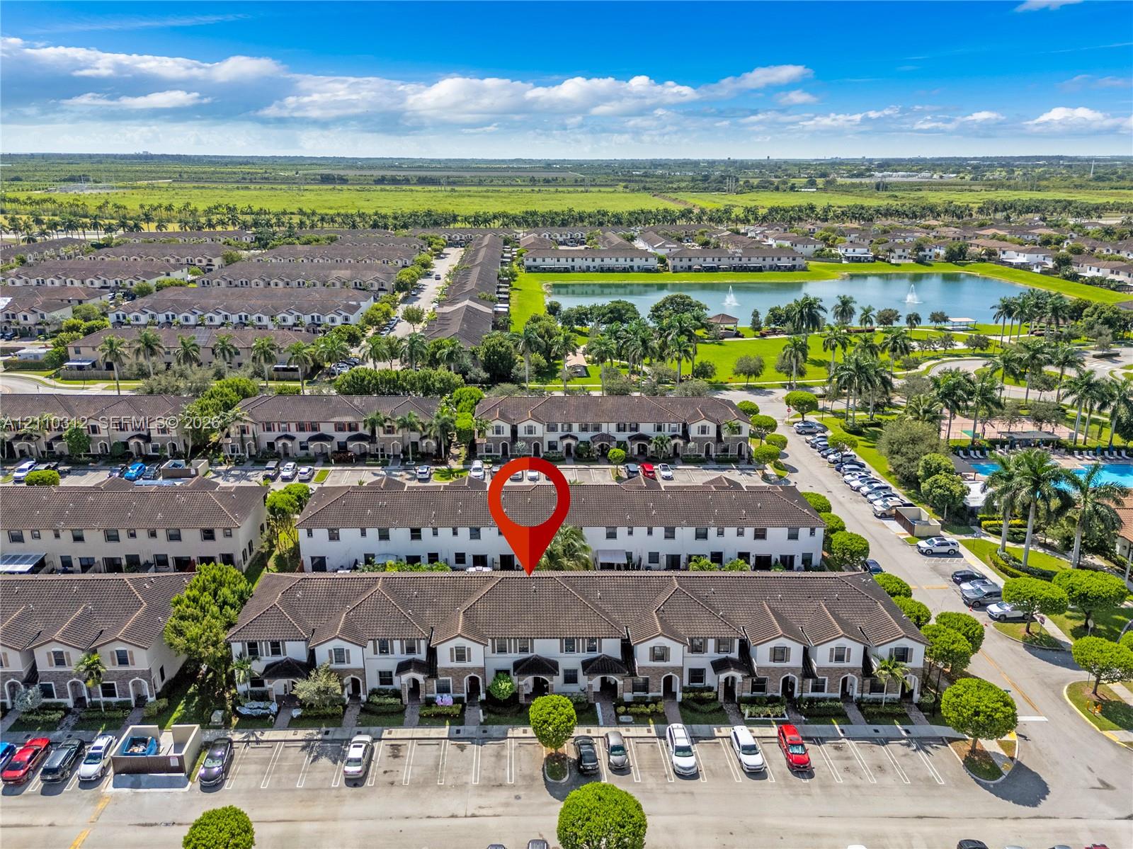 Aerial perspective of a multi-unit residential building featuring a multi-gabled roofline, light-toned stucco exterior, and dedicated surface parking