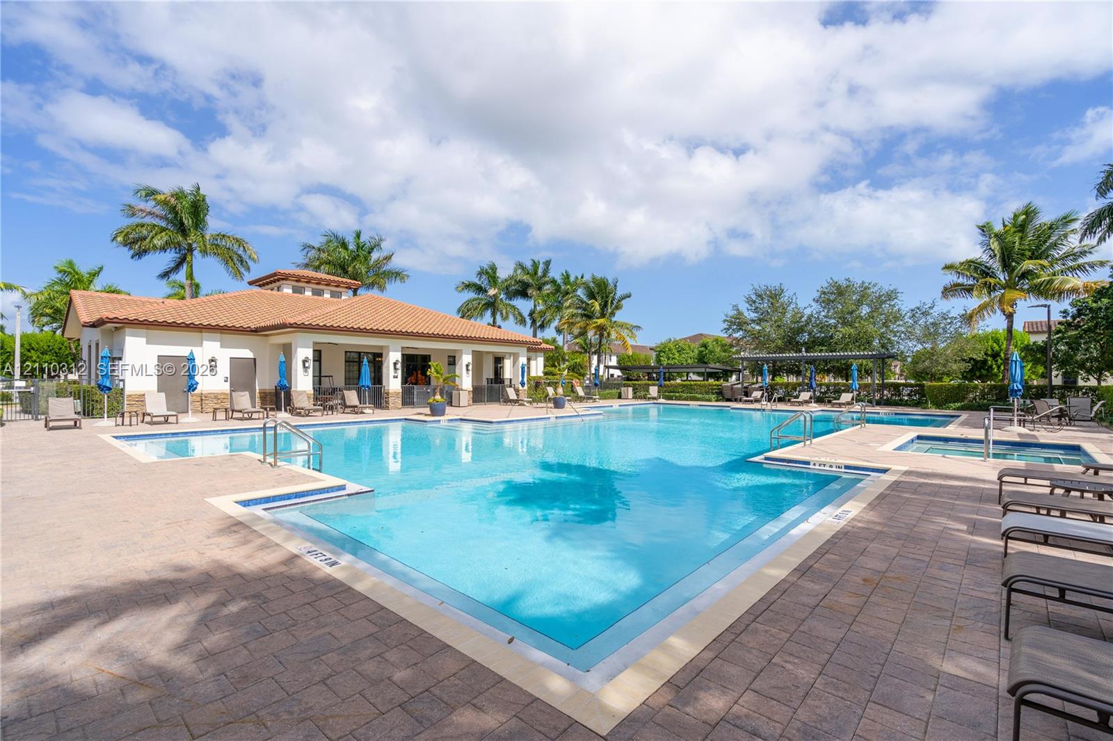 Resort-style pool featuring a paver stone deck, integrated spa, built-in staircase entry, and surrounding palm trees