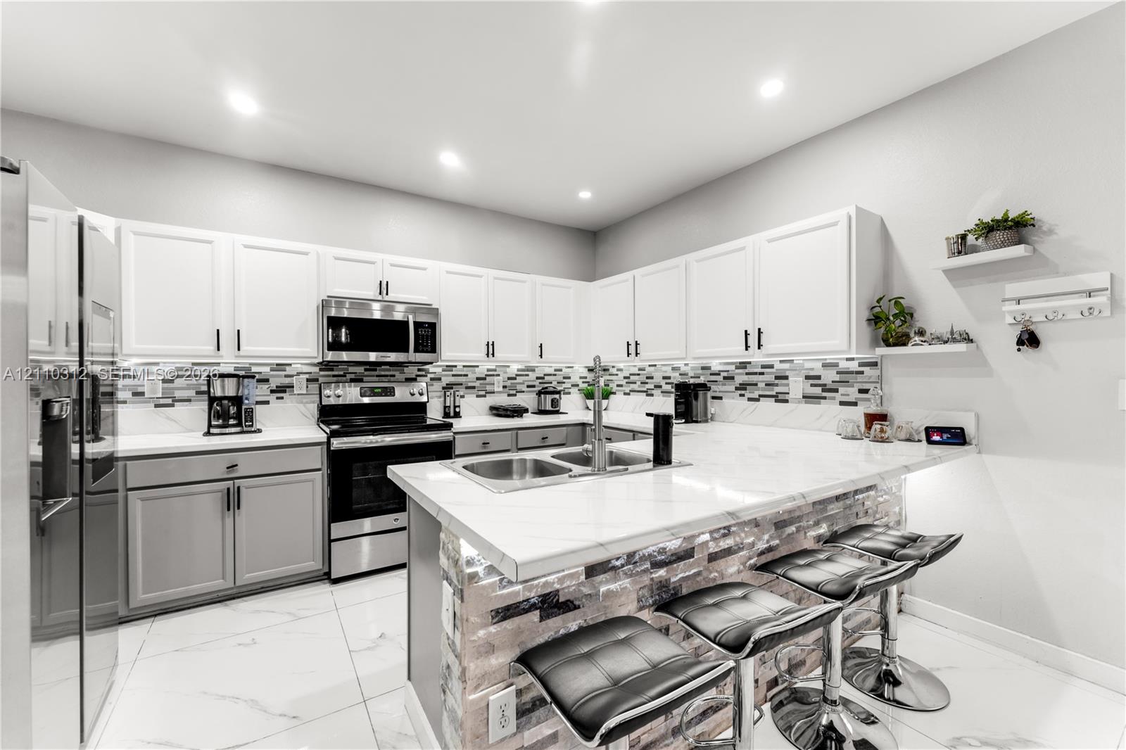 Kitchen featuring white upper cabinetry, grey lower cabinetry, white stone-finish countertops, stainless steel appliances, and a tiled backsplash