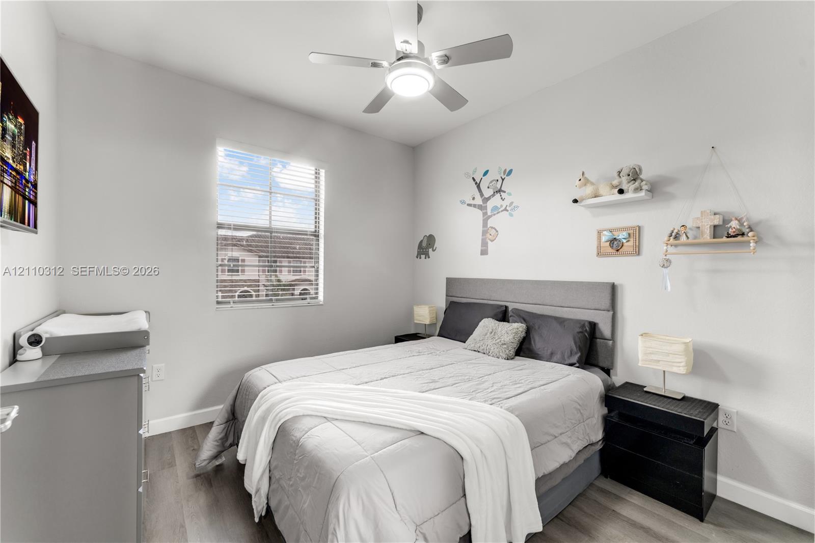 Bedroom featuring wood-finish flooring, a neutral color palette, a single-pane window with horizontal blinds, and a ceiling-mounted light fixture with an integrated fan