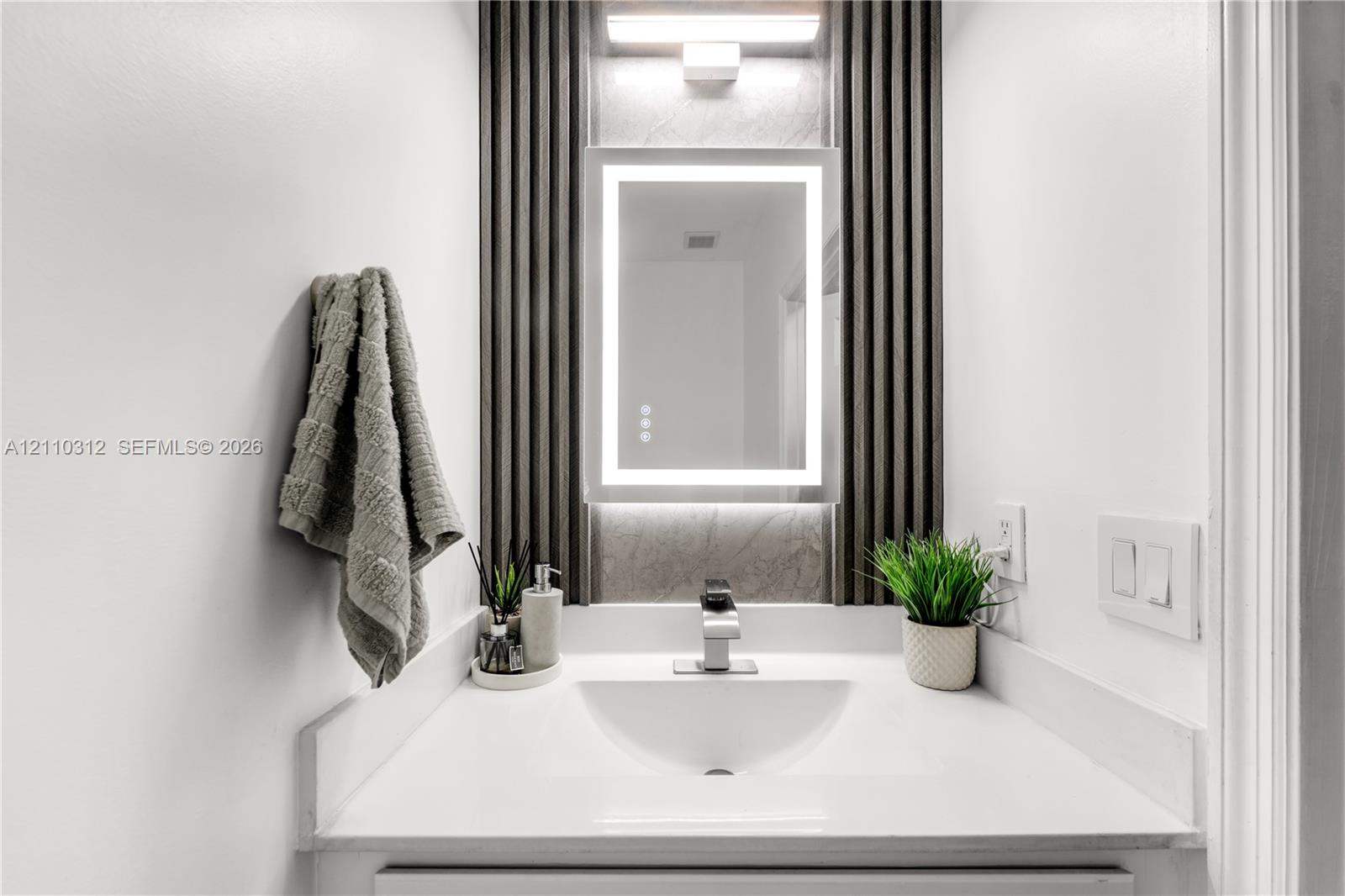Integrated vanity featuring a solid surface countertop, undermount sink, LED-lit vanity mirror, and decorative fluted wall paneling