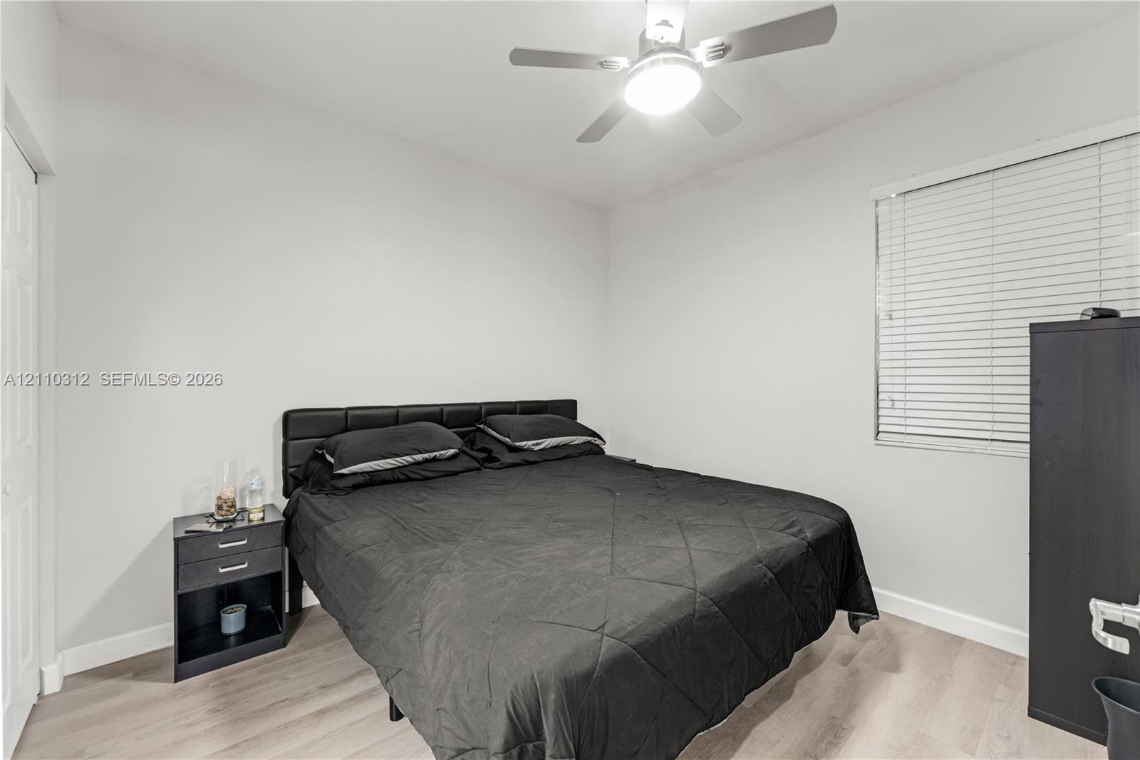 Interior room featuring wood-finish flooring, white walls, horizontal window blinds, and a ceiling fan with integrated light fixture