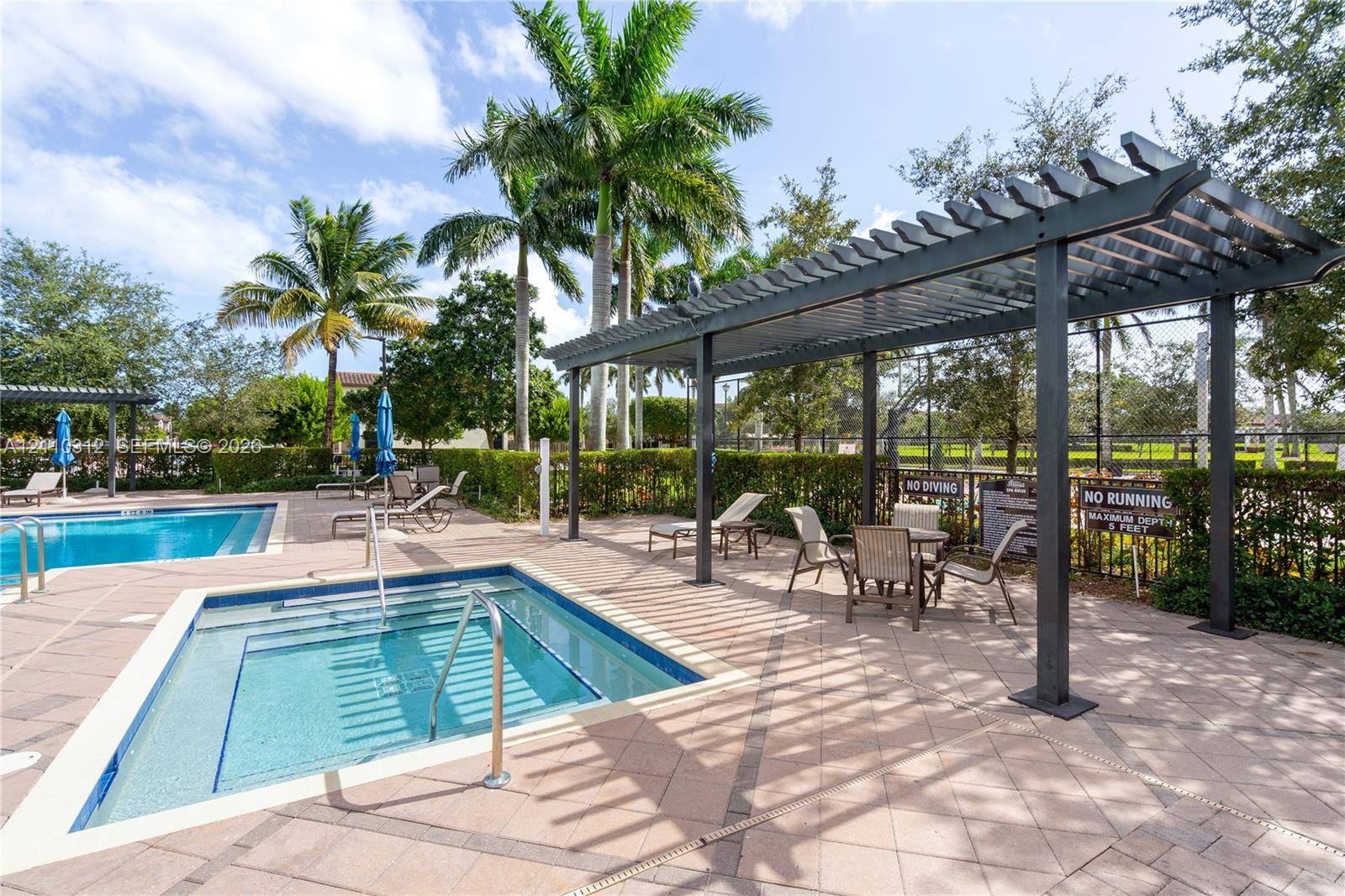Outdoor area featuring an in-ground pool and spa, stone-paver decking, metal pergola, and perimeter privacy hedging