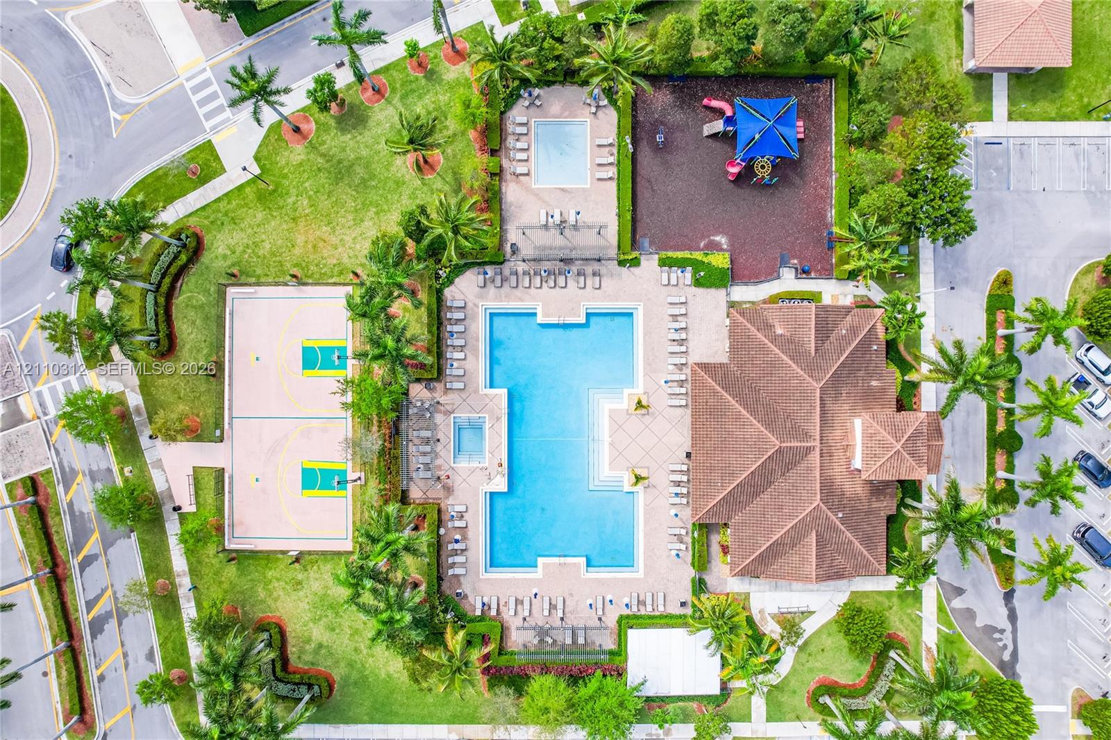 Aerial perspective of a community recreation facility featuring a swimming pool, spa, basketball court, playground, and multi-faceted clubhouse building