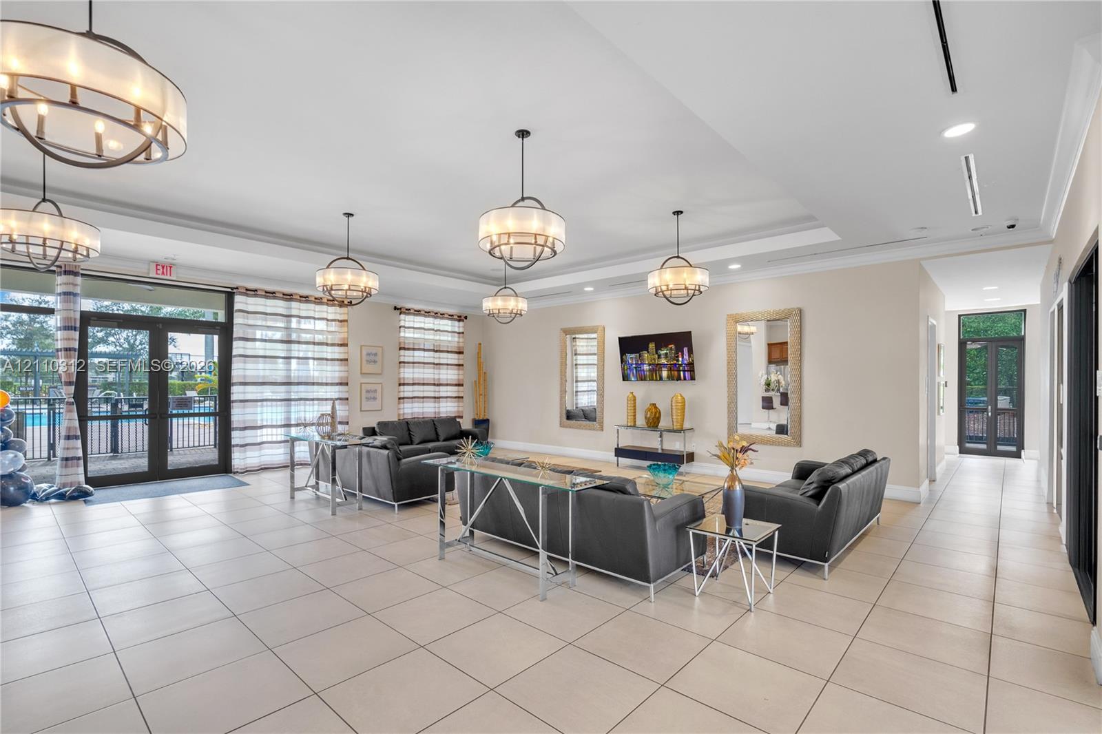 Large-format tile flooring, tray ceilings, multiple tiered drum chandeliers, recessed lighting, and expansive glass-paneled entry doors