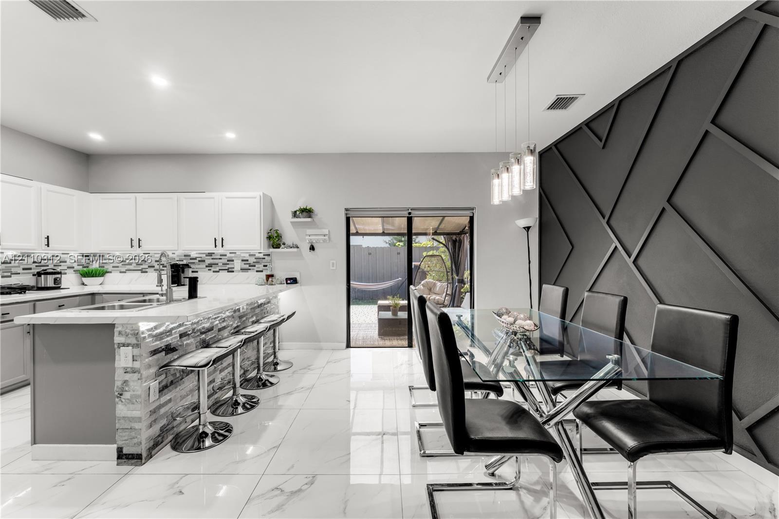 Kitchen featuring white cabinetry, stone-finish countertops, a multi-textured stone backsplash, glossy tile flooring, and an accent wall with geometric millwork