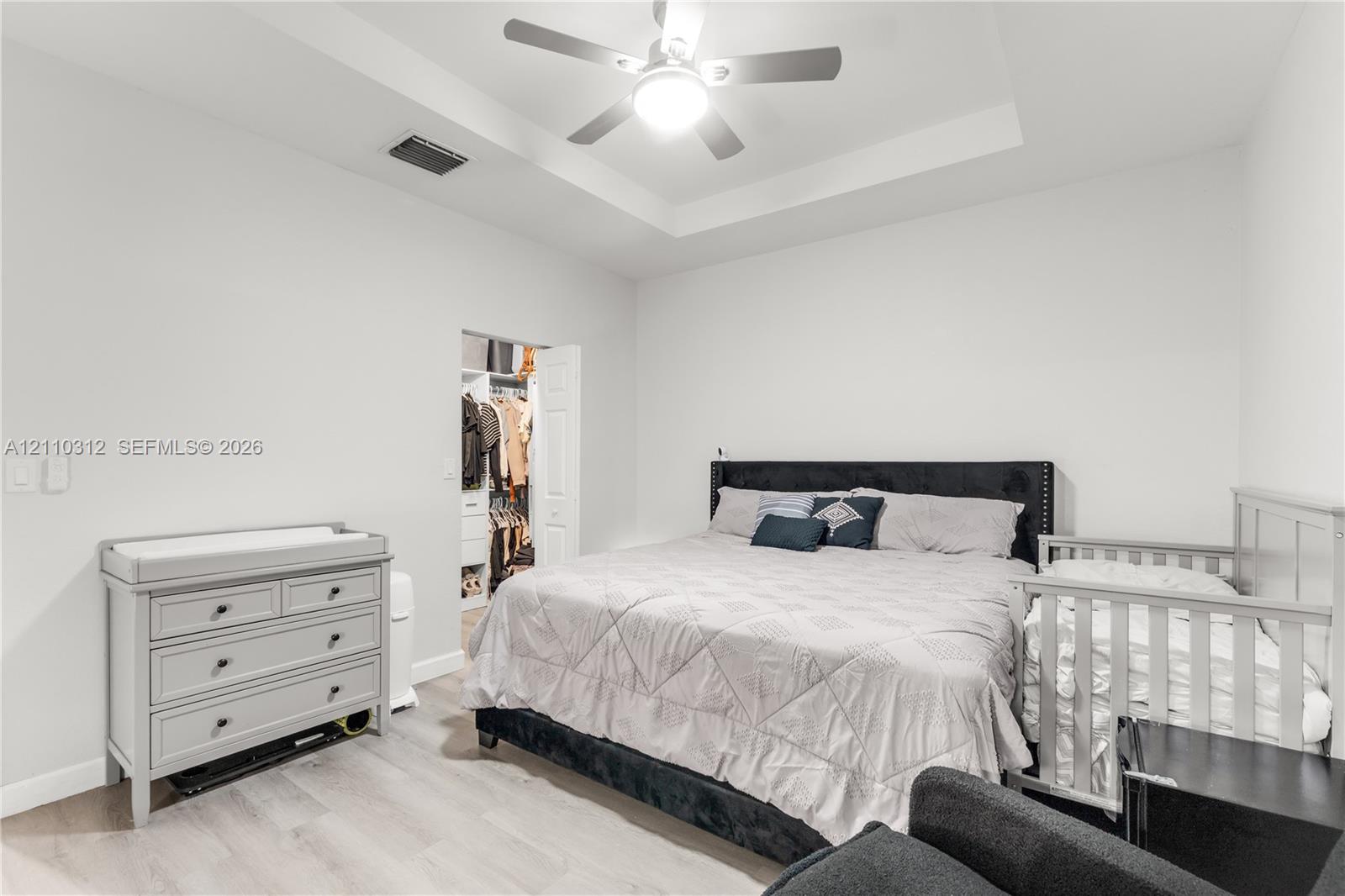 Tray ceiling featuring a central light-integrated ceiling fan, neutral wall finishes, wood-finish flooring, and a walk-in closet with built-in shelving