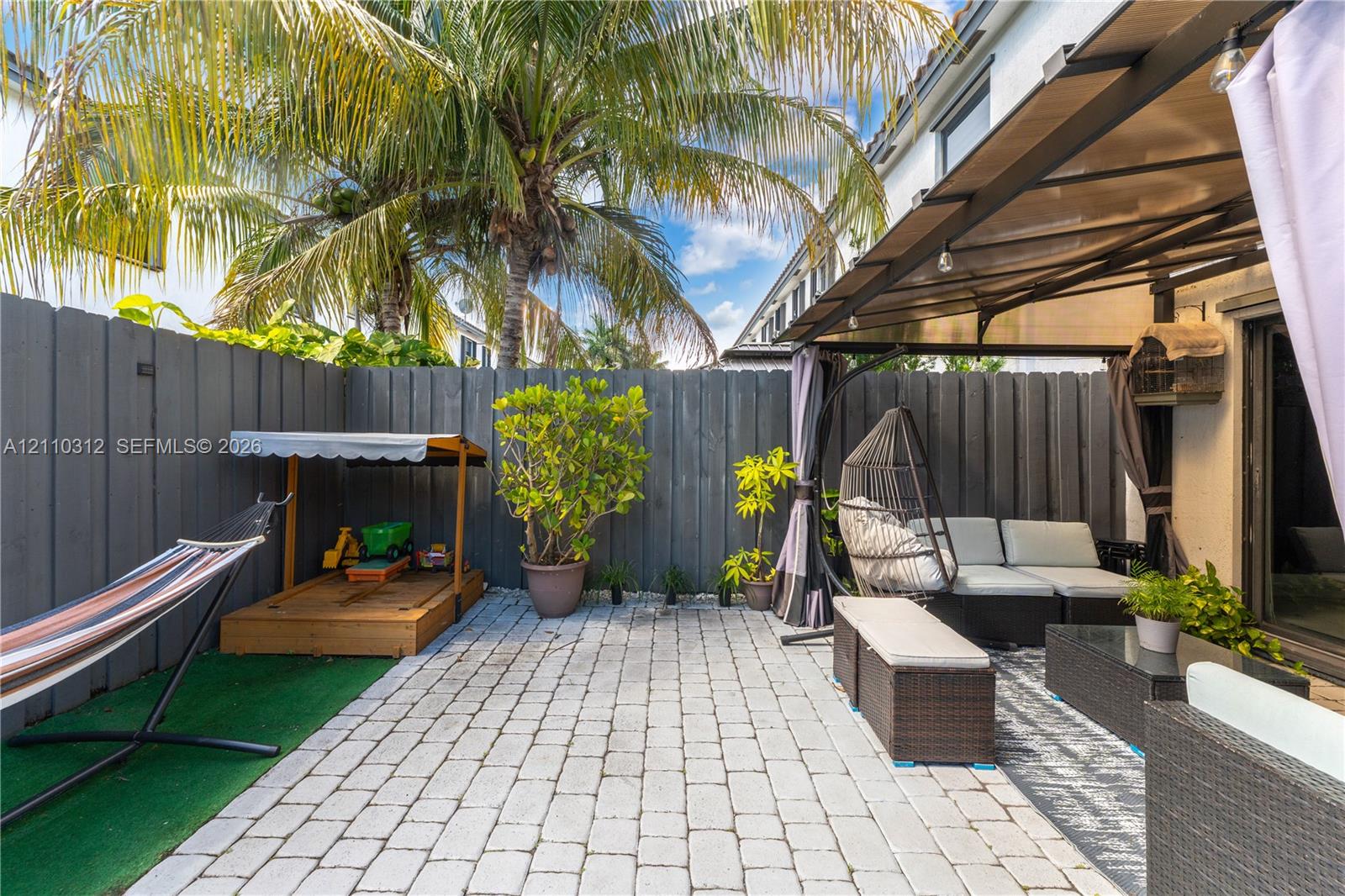 Private patio featuring stone paver flooring, overhead metal-framed structure, and full-height perimeter fencing