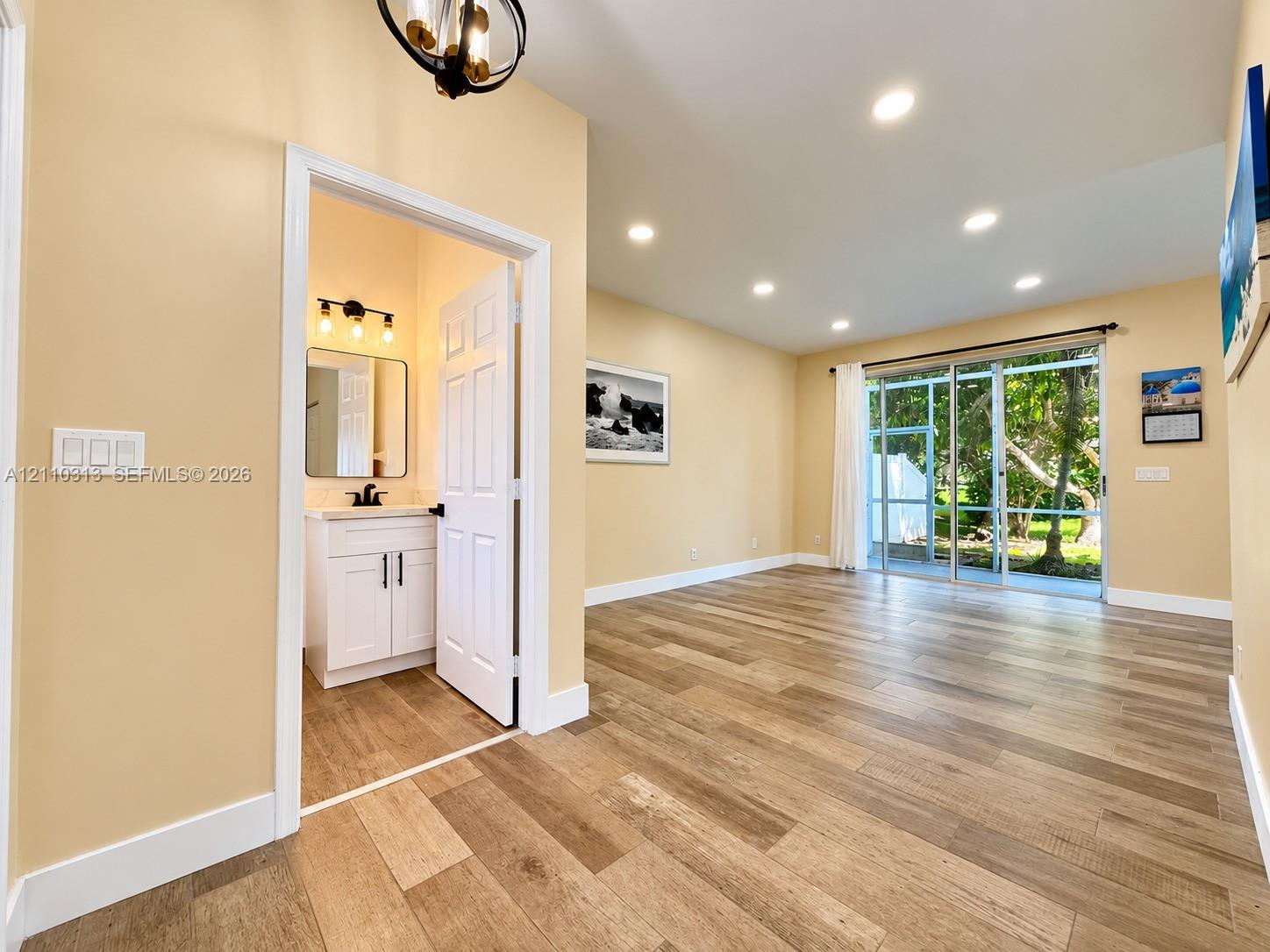Wood-finish tile flooring throughout with recessed lighting, floor-to-ceiling sliding glass doors, and a bathroom featuring a white vanity cabinet and matte black hardware