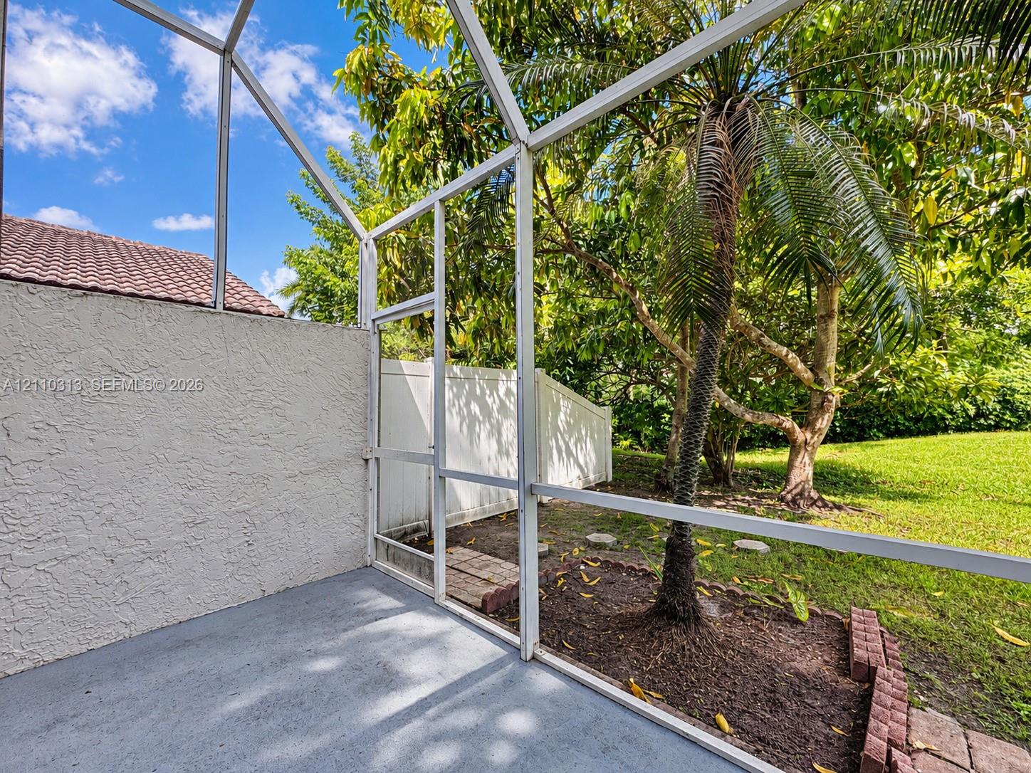 Screened-in patio featuring a concrete floor, stucco wall, white aluminum framing, and direct access to a grassy yard with mature palms and vinyl privacy fencing