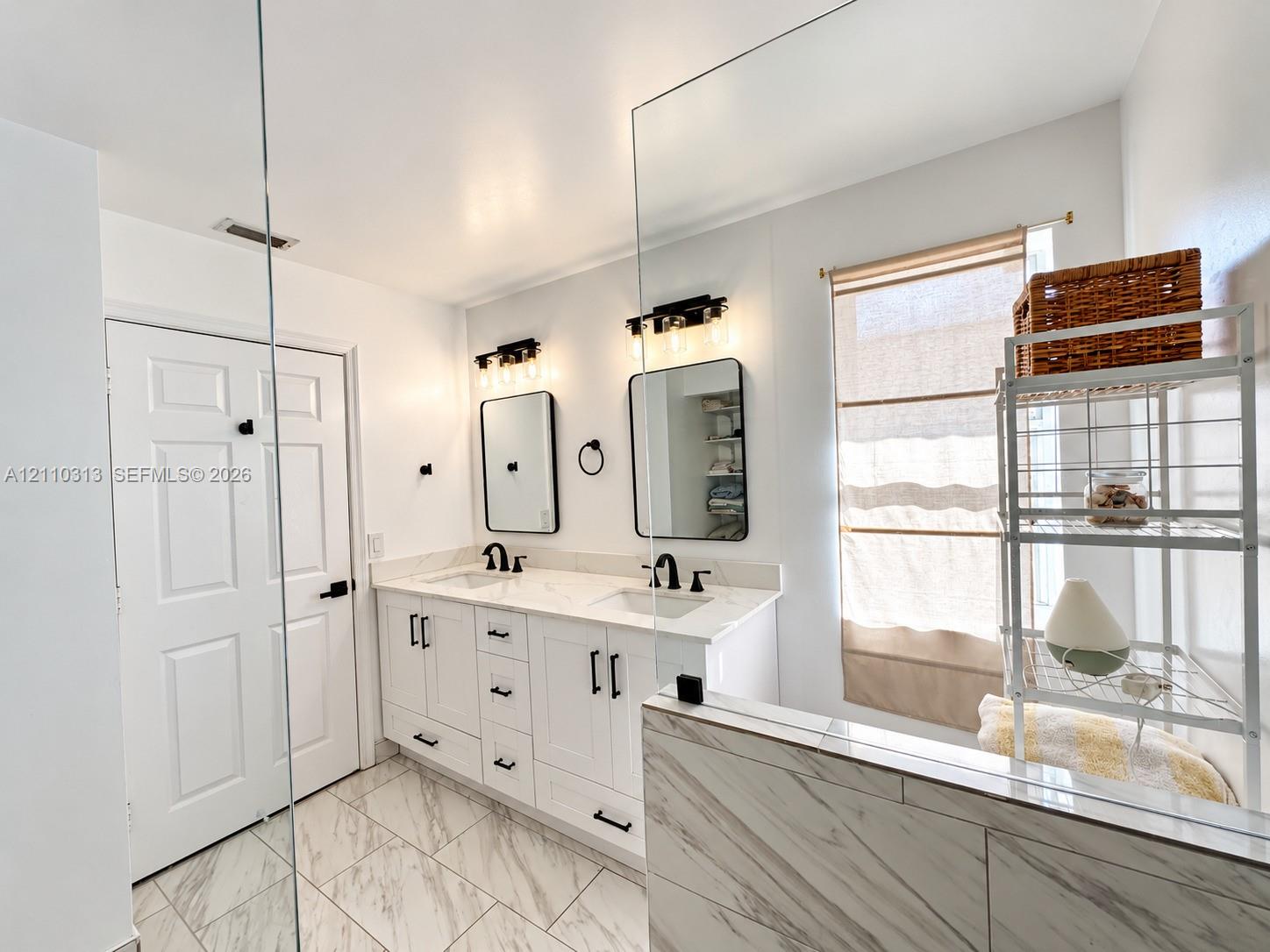 Dual-sink vanity with white cabinetry, light-toned stone-finish countertops, rectangular undermount sinks, matte black fixtures, and framed mirrors